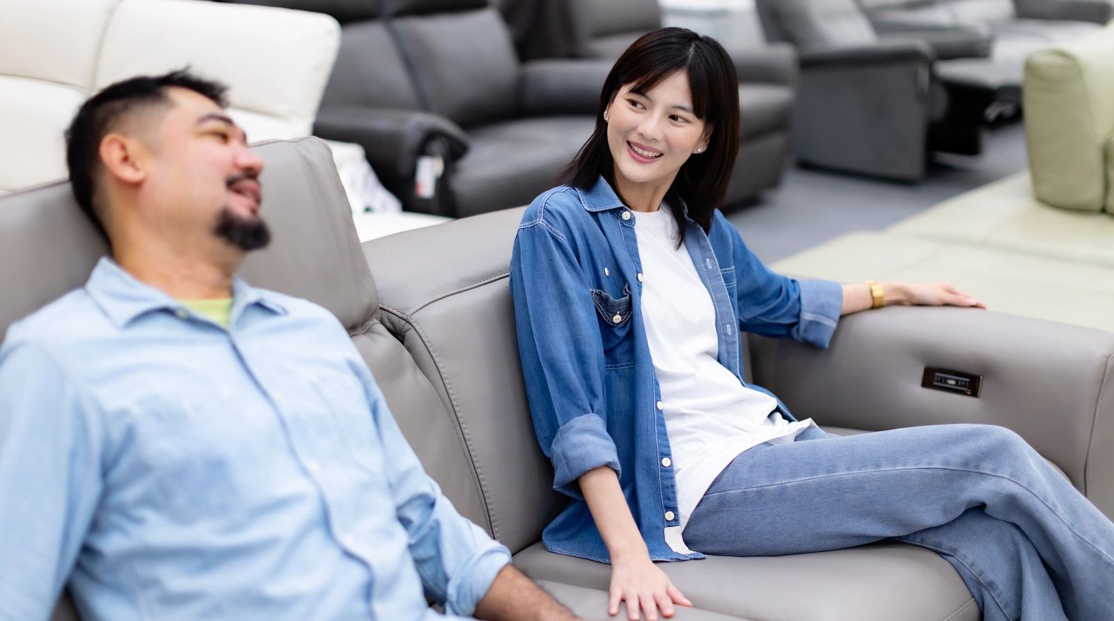 A couple sits on a sofa in a furniture showroom testing the comfort and fit before purchasing. Physically sitting on a sofa is one of the best ways to evaluate upholstery, cushion support, and overall construction when shopping for floor sample furniture.