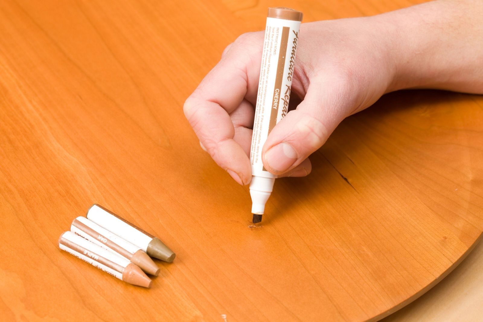 Using a wood touch-up marker to repair a small scratch on a wooden table — minor imperfections like this often lead to the best furniture deals.