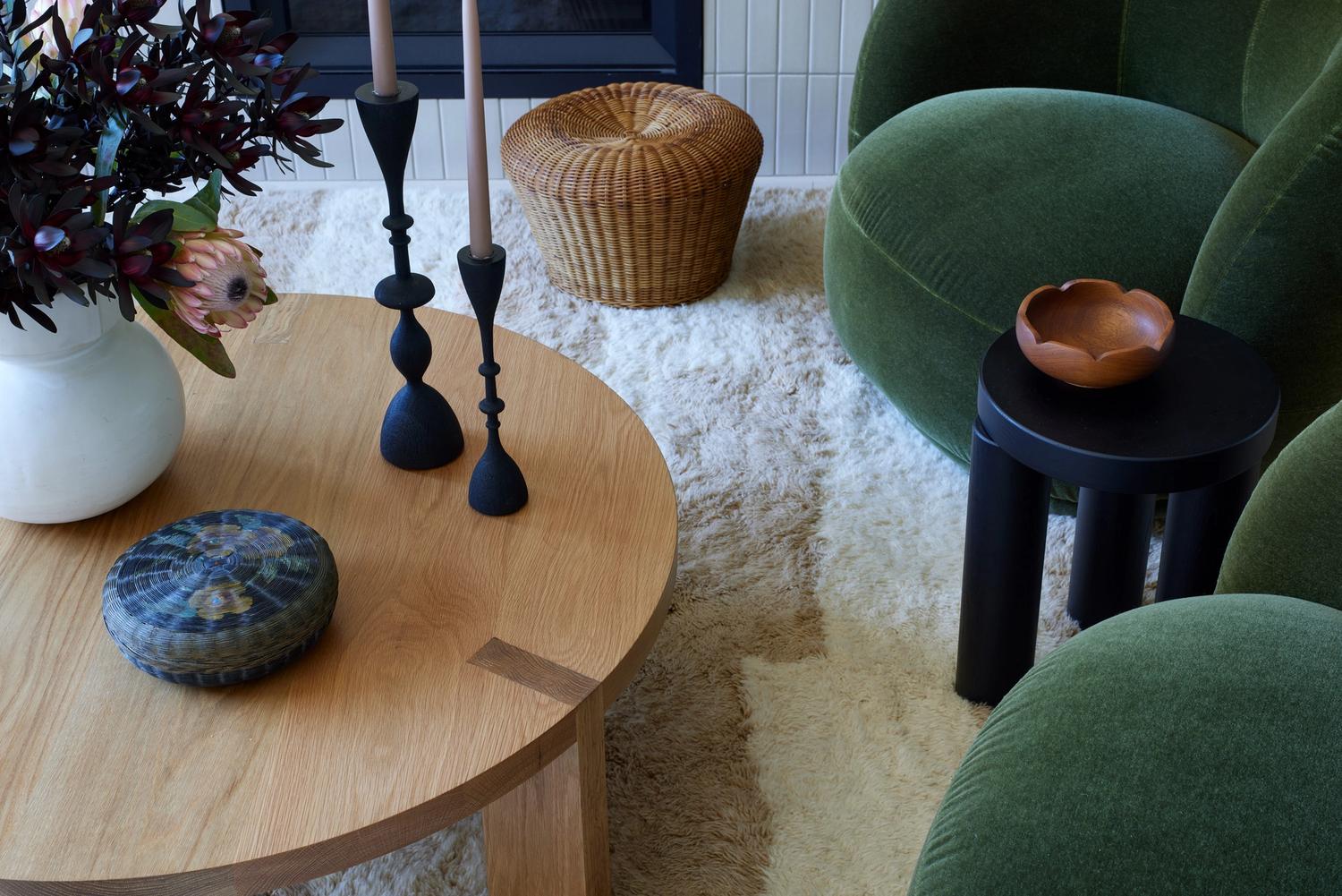 Modern living room with round wood table, neutral rug and green velvet chairs