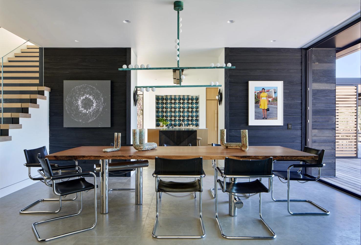 Dining area with warm wood table, vintage chairs, modern art, and silver metal accents throughout