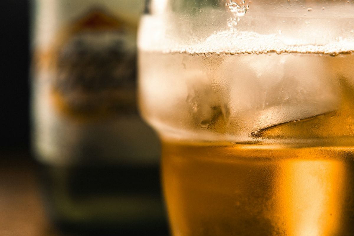 An ice-cold glass of ginger beer with lime beside a chilled bottle