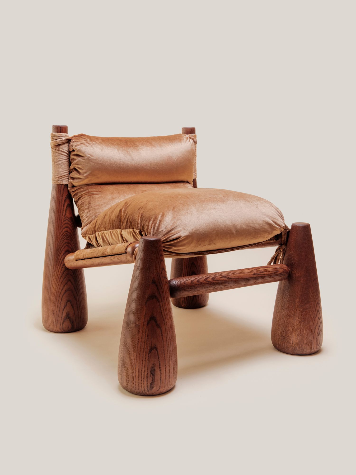 A warm-toned lounge chair with rounded wooden legs and plush velvet cushions, ANGLED VIEW in a cozy living room beside a wooden side table with a vase.