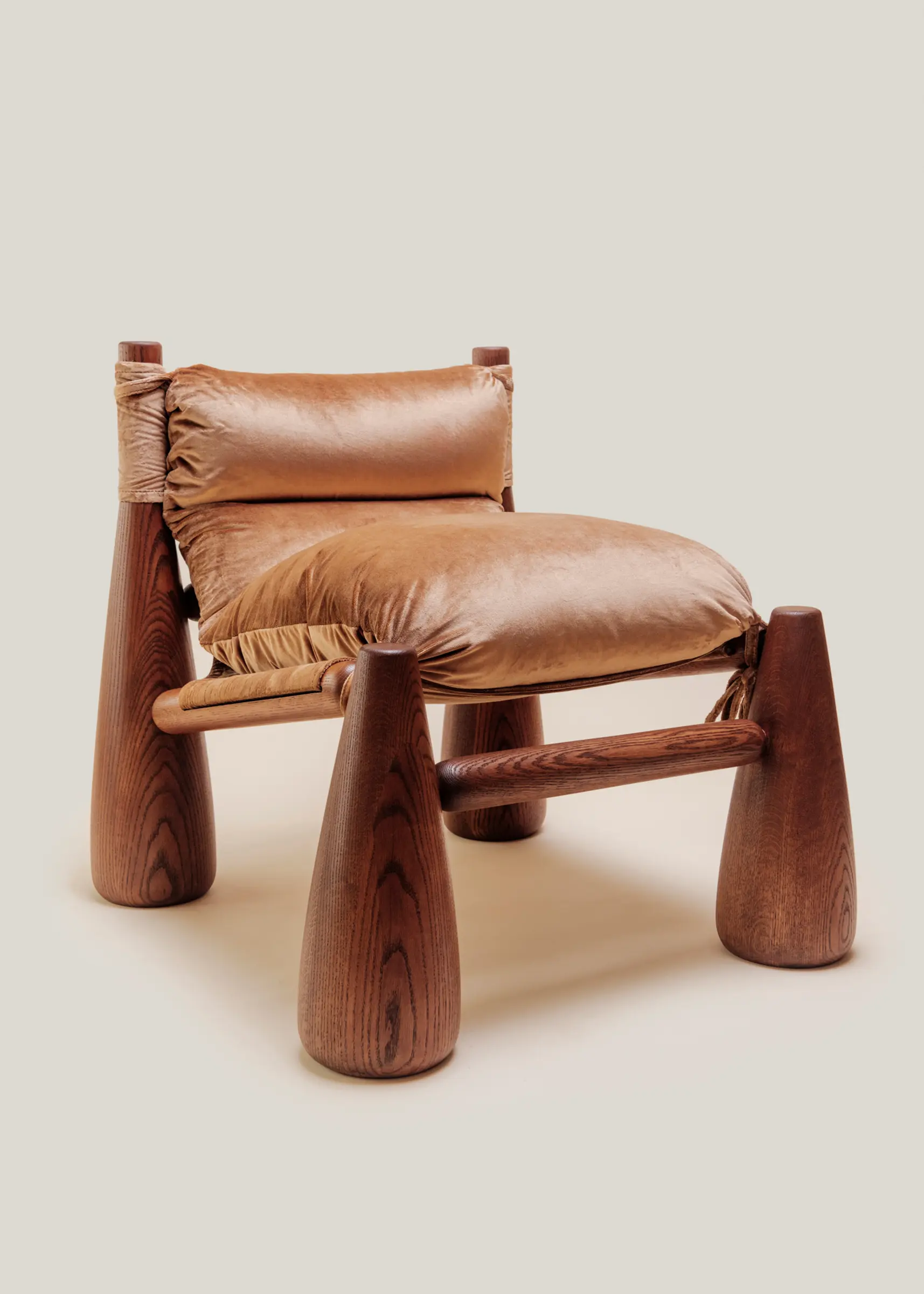 A warm-toned lounge chair with rounded wooden legs and plush velvet cushions, ANGLED VIEW in a cozy living room beside a wooden side table with a vase.