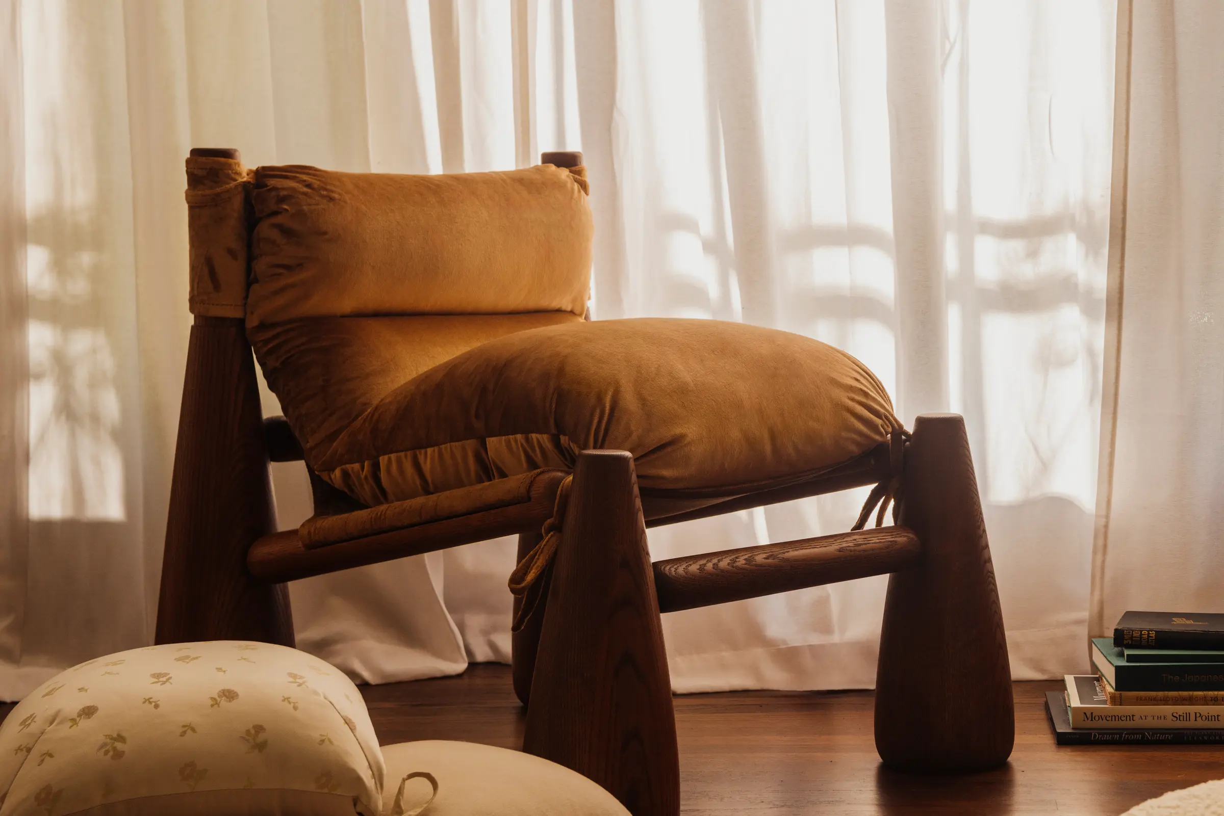 A living room with a brown Bell Chair, cushions on the floor, and a large vase of blossoming branches.