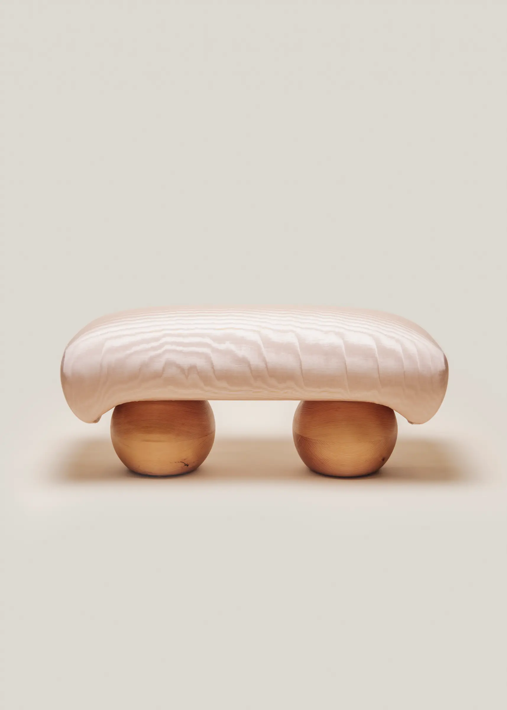 Minimalist front view of the Mini Orb Bench by Studio Sam Klemick, featuring a soft quilt-like seat resting on two rounded wooden spheres.