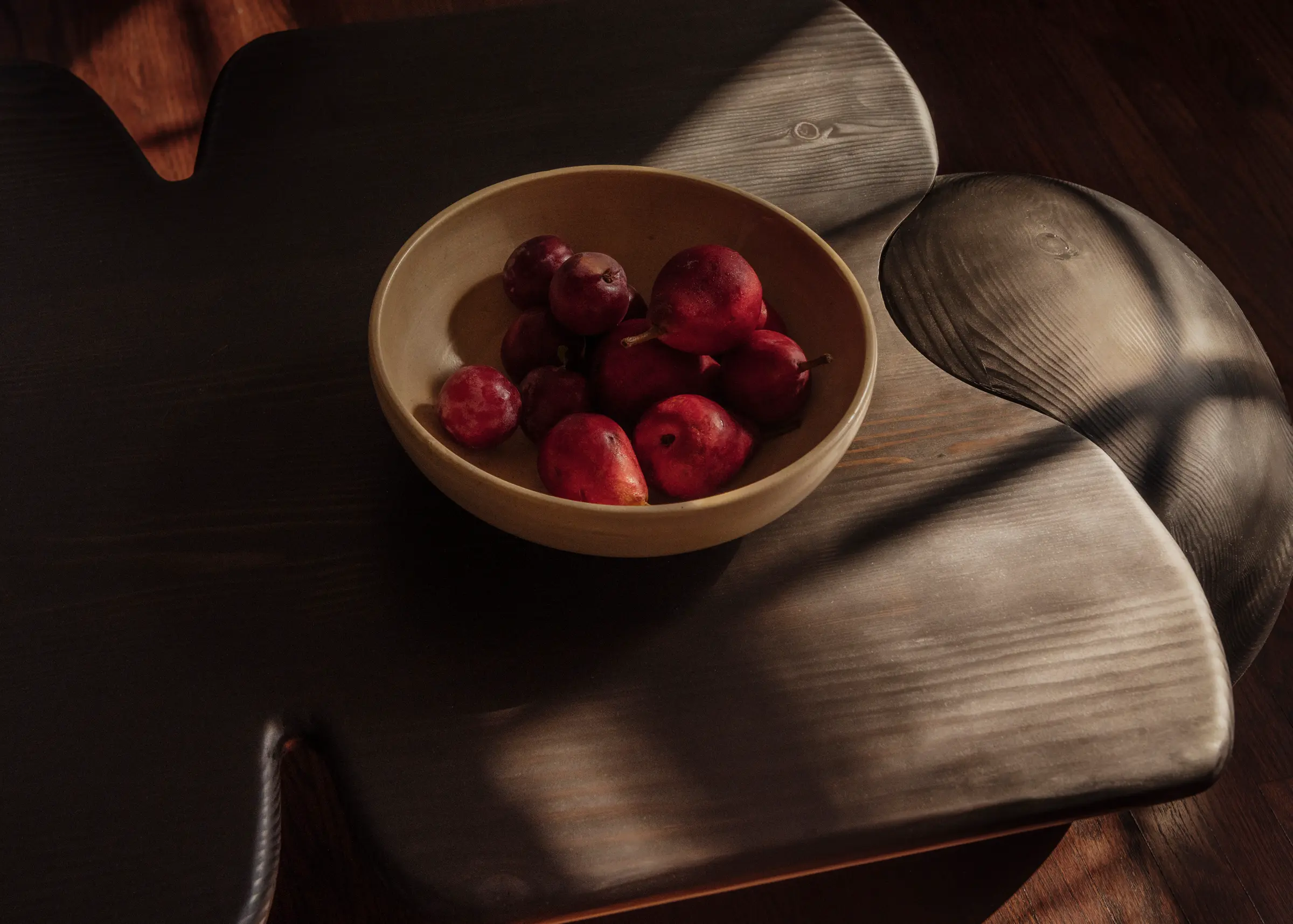Dark wood table with bowl of red pears on it.
