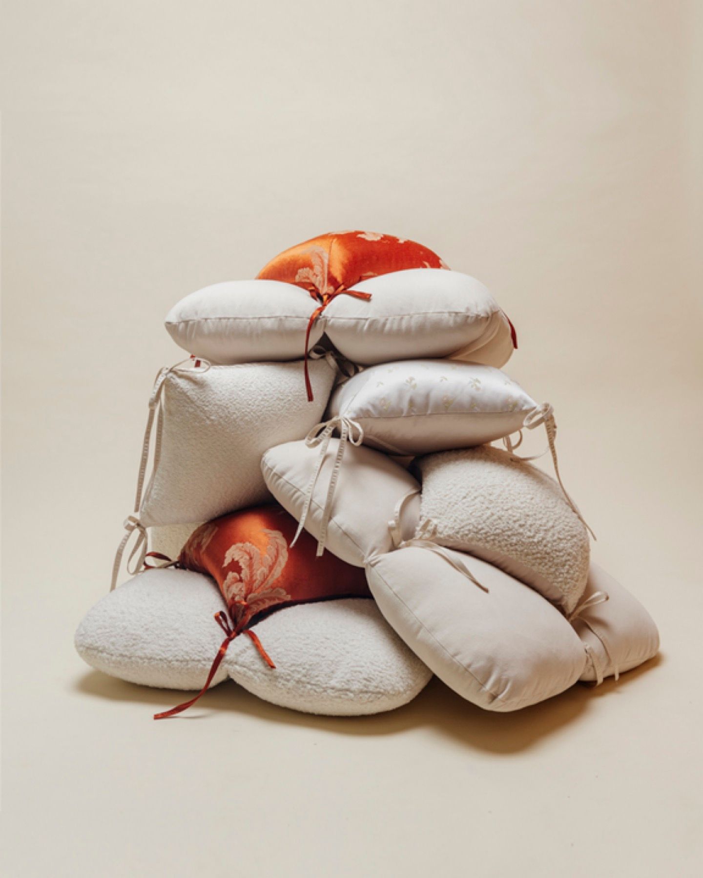A large, aesthetic pile of various decorative cushions in white, cream, and burnt orange jacquard fabrics.