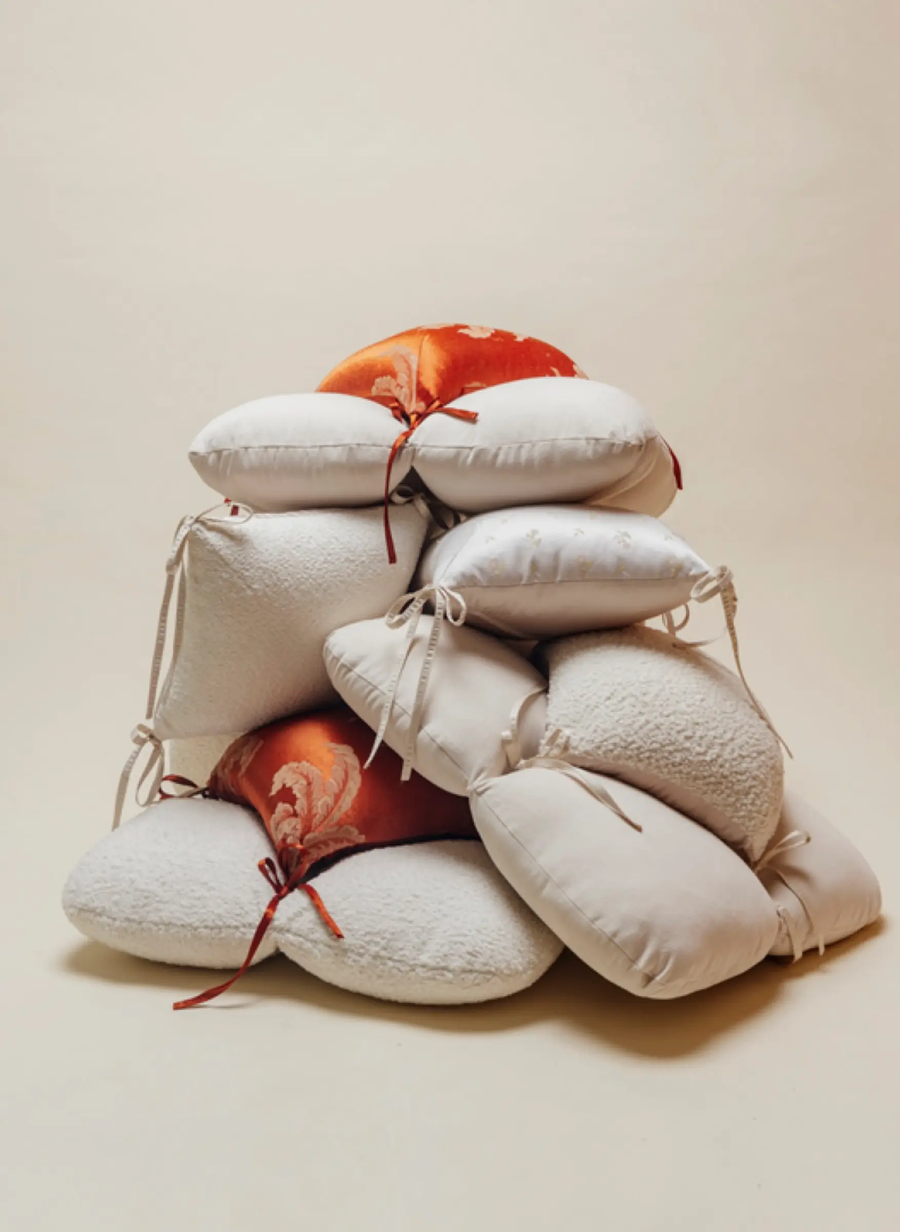 A large, aesthetic pile of various decorative cushions in white, cream, and burnt orange jacquard fabrics.