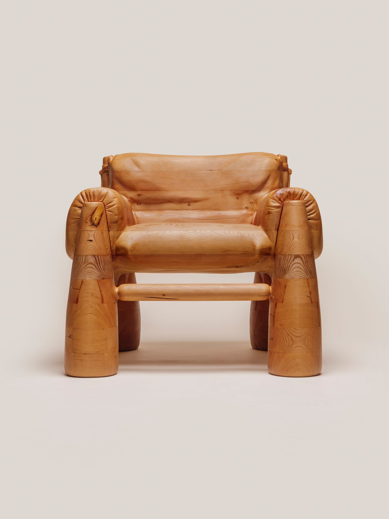 A large wooden armchair that is skillfully carved to look like a soft, overstuffed upholstered chair.