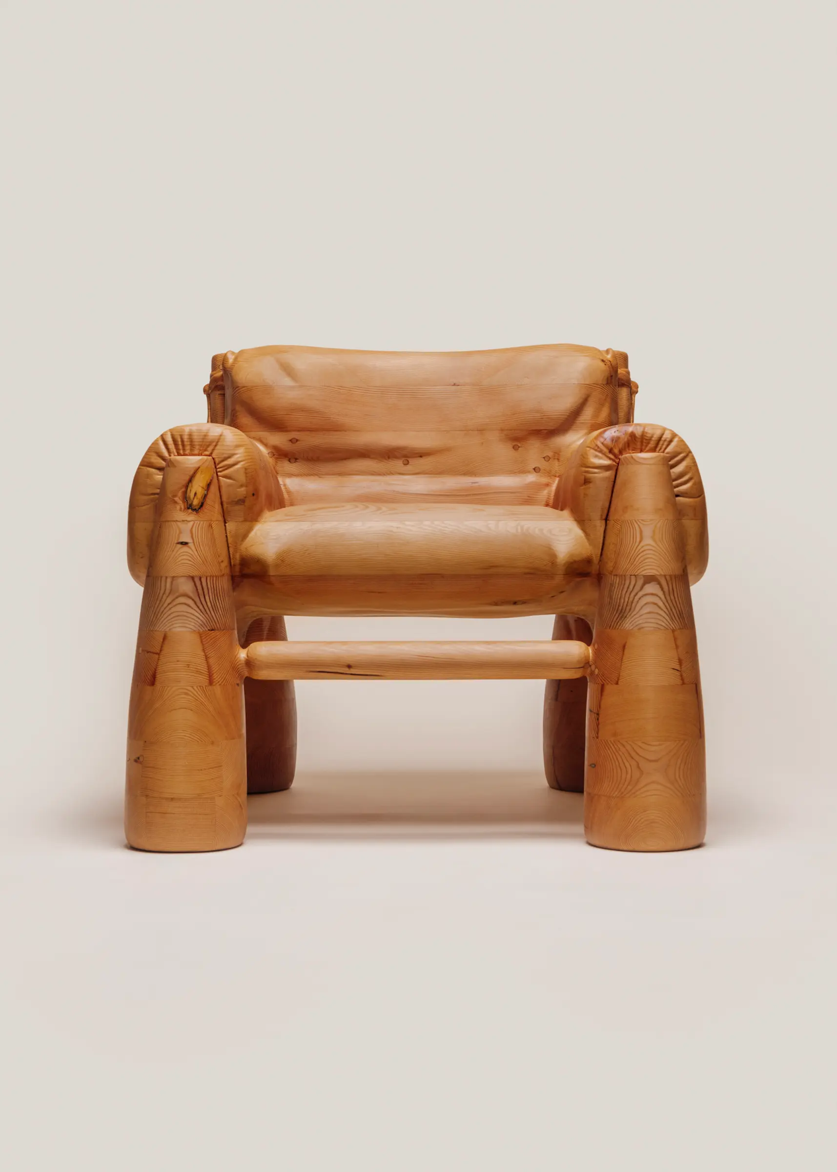 A large wooden armchair that is skillfully carved to look like a soft, overstuffed upholstered chair.