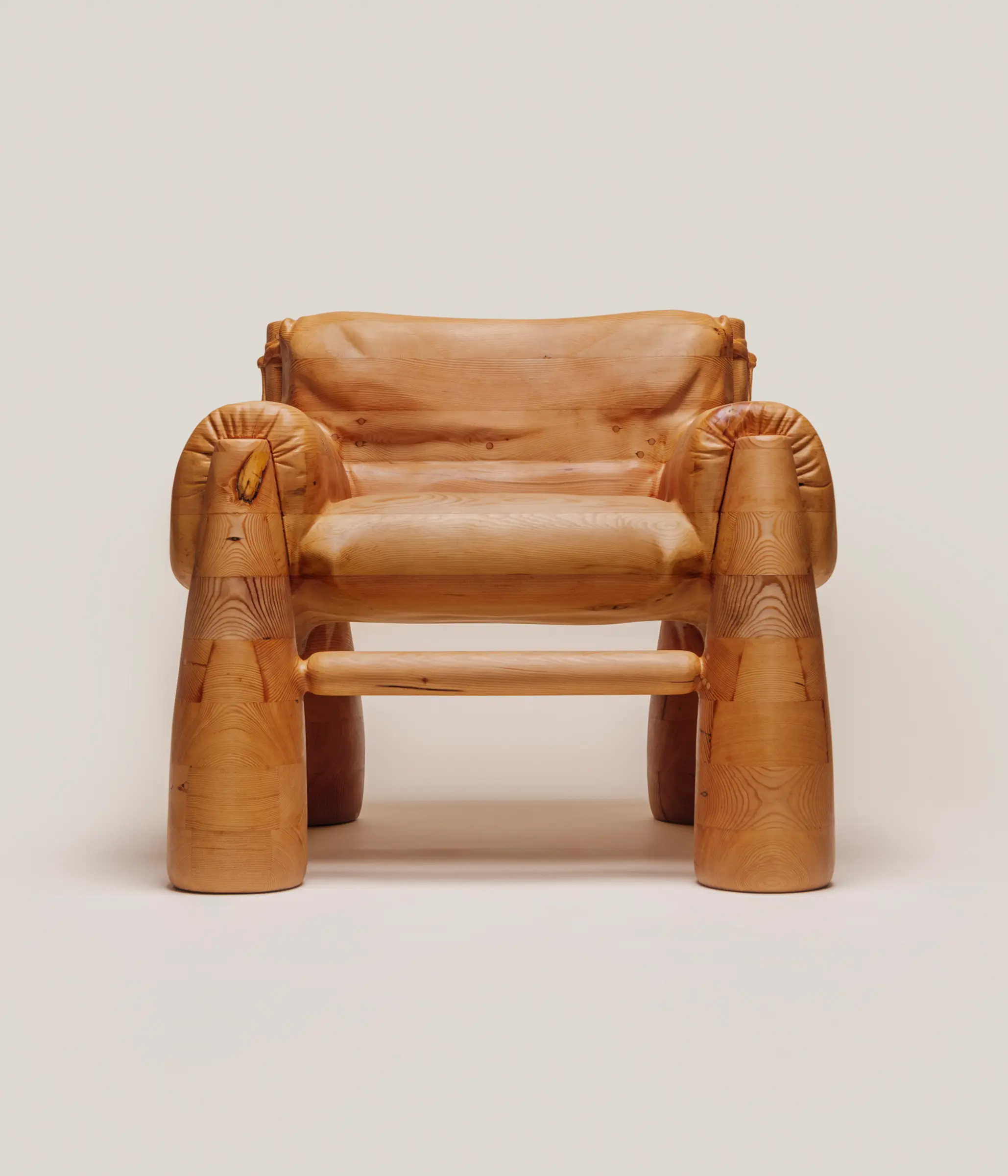 A large wooden armchair that is skillfully carved to look like a soft, overstuffed upholstered chair.