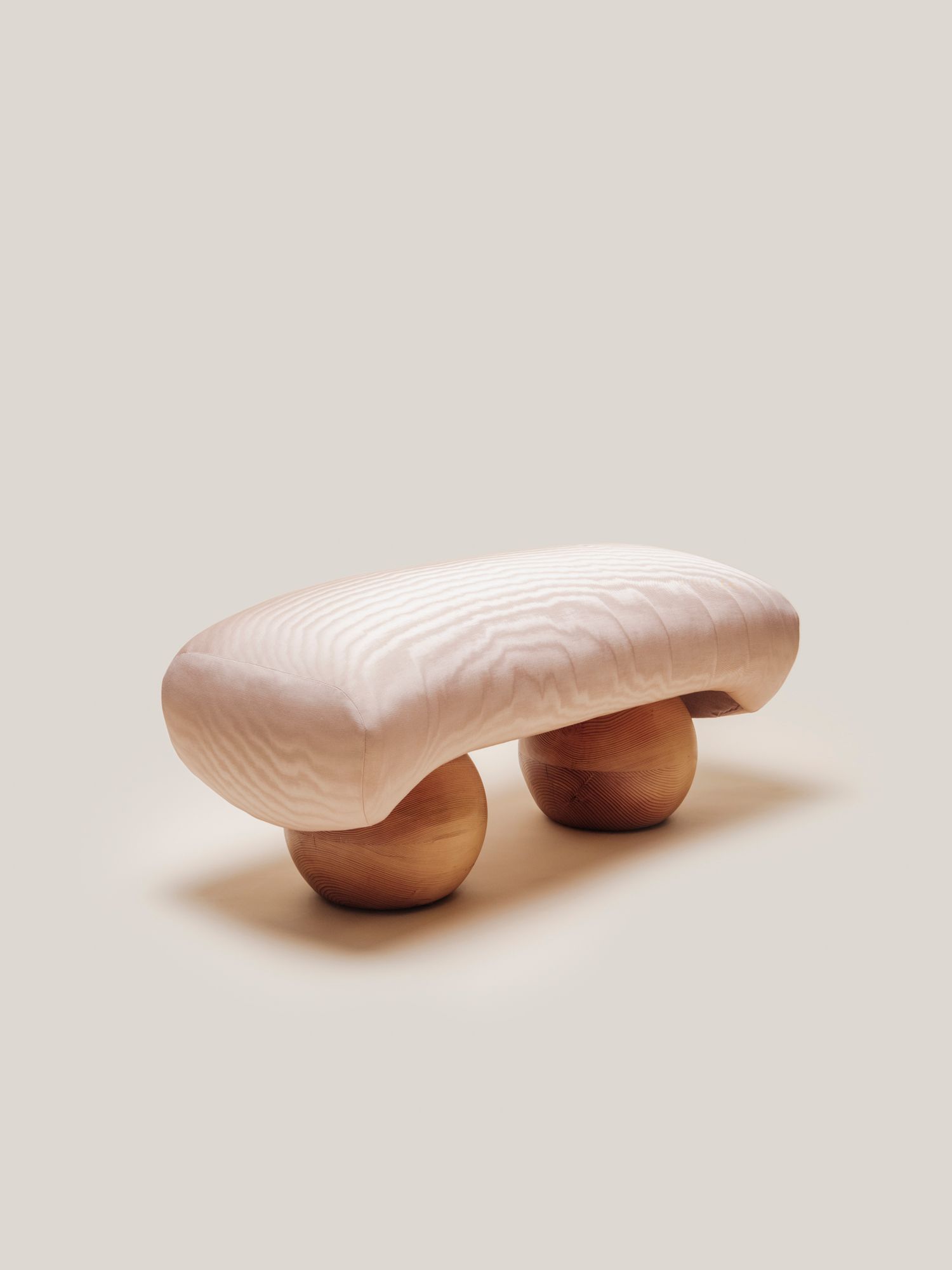 Minimalist front view of the Mini Orb Bench by Studio Sam Klemick, featuring a soft quilt-like seat resting on two rounded wooden spheres.