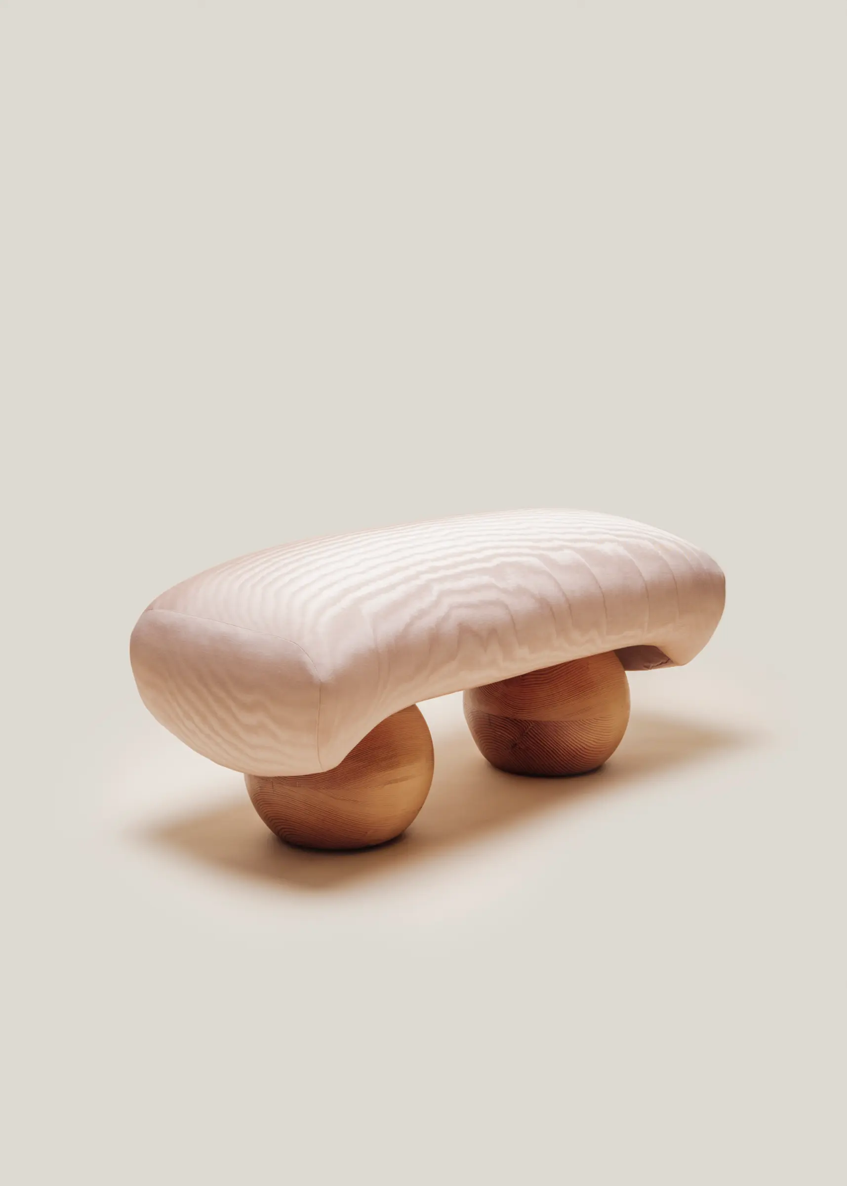 Minimalist front view of the Mini Orb Bench by Studio Sam Klemick, featuring a soft quilt-like seat resting on two rounded wooden spheres.