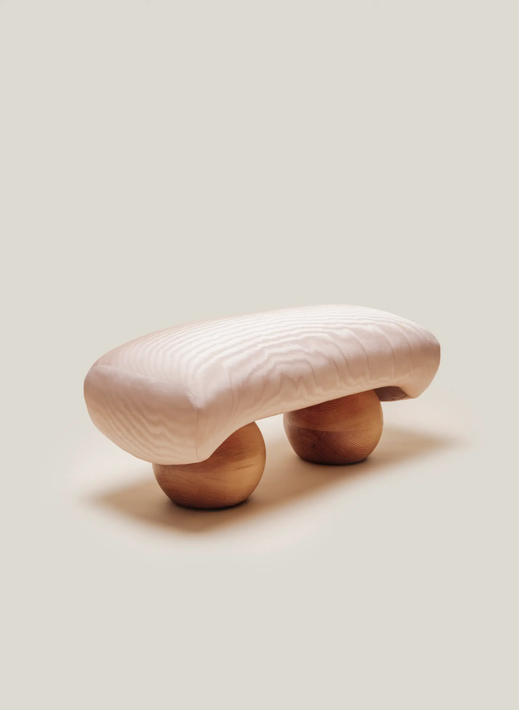 Minimalist front view of the Mini Orb Bench by Studio Sam Klemick, featuring a soft quilt-like seat resting on two rounded wooden spheres.
