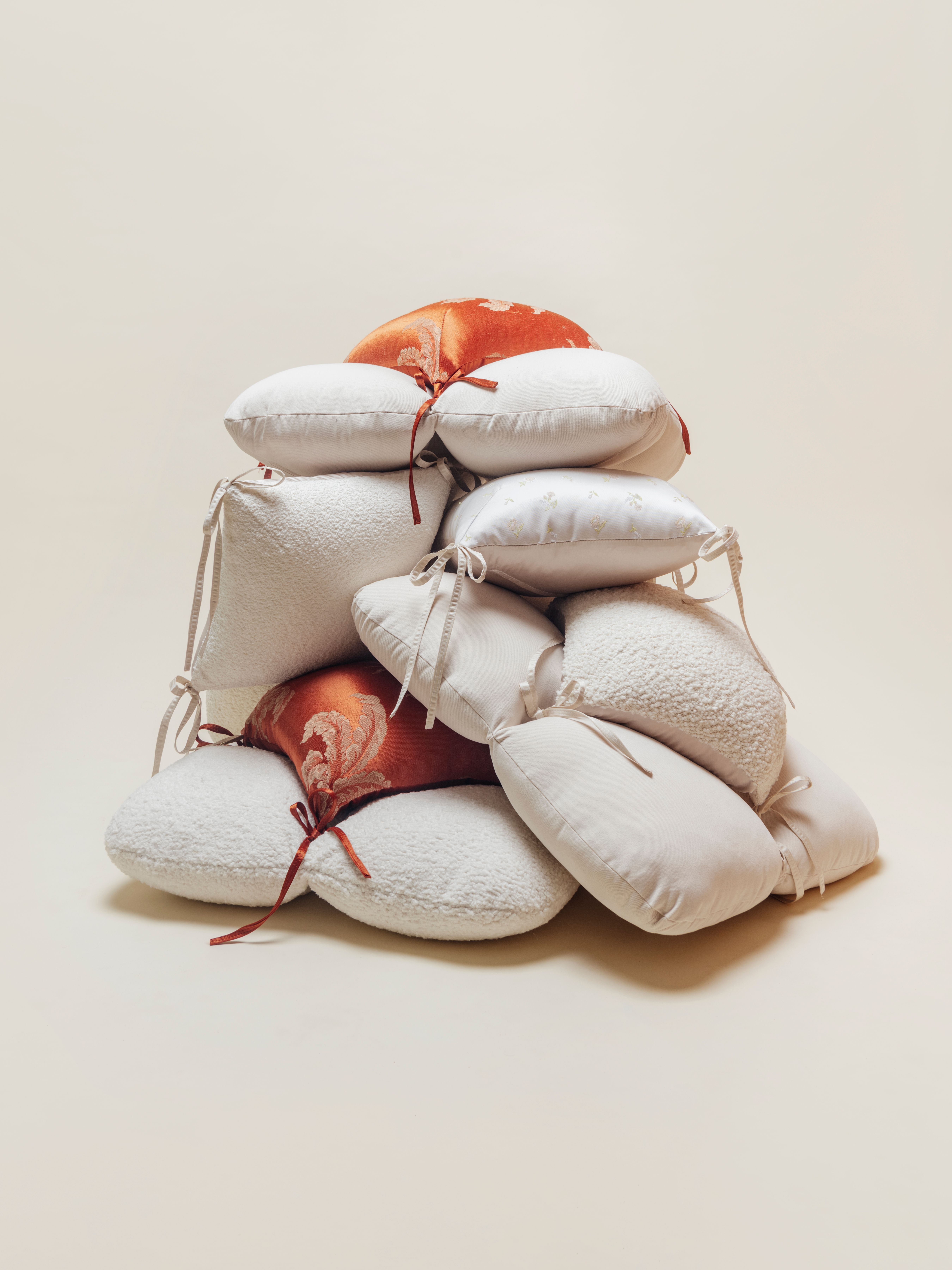 A large, aesthetic pile of various decorative cushions in white, cream, and burnt orange jacquard fabrics.