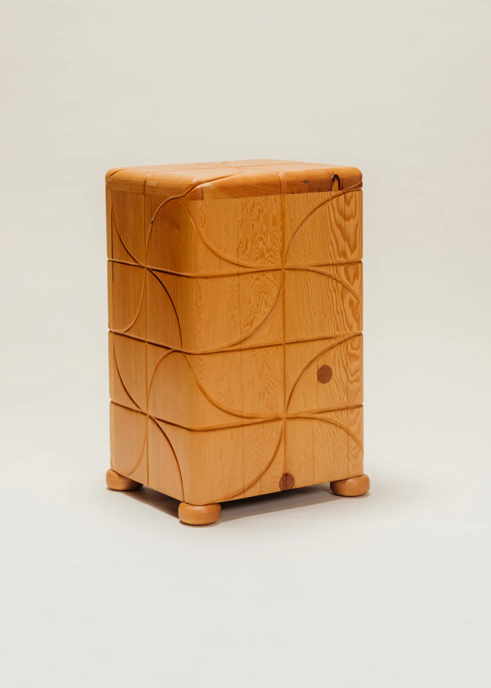 Wooden side table with a polished finish and carved pinwheel-inspired geometric patterns on all sides, standing on short rounded feet against a neutral background.