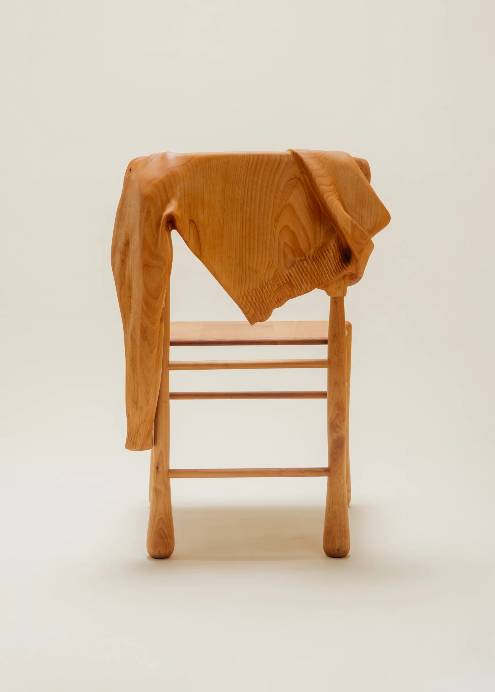 back of wooden chair with wood sweater hanging over it on a clean background.