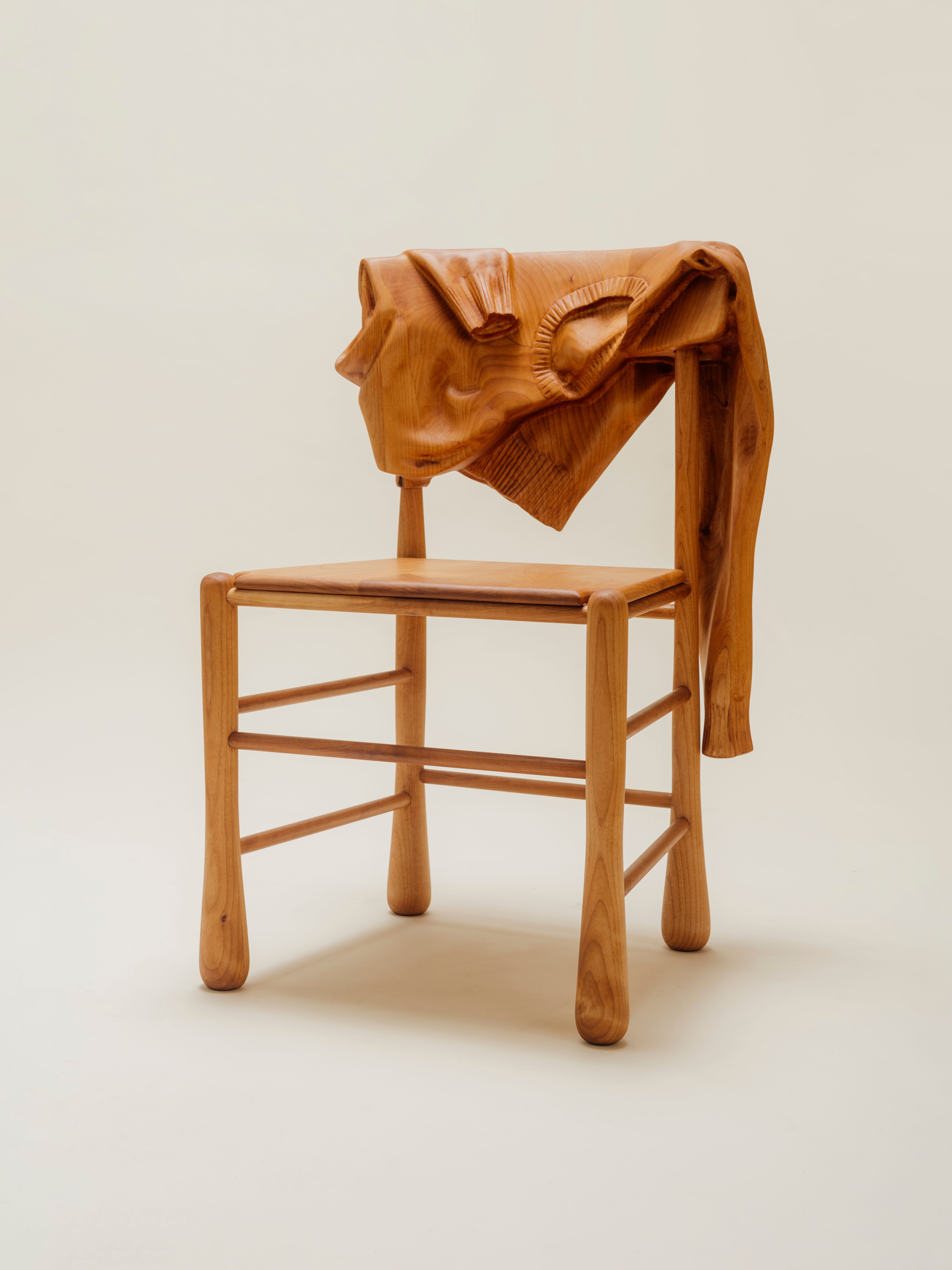 Front of wooden chair with wood sweater hanging over it on a clean background.