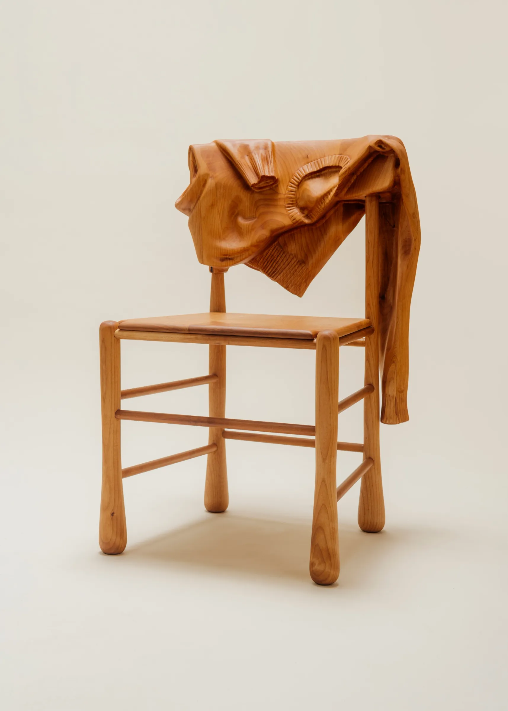 Front of wooden chair with wood sweater hanging over it on a clean background.
