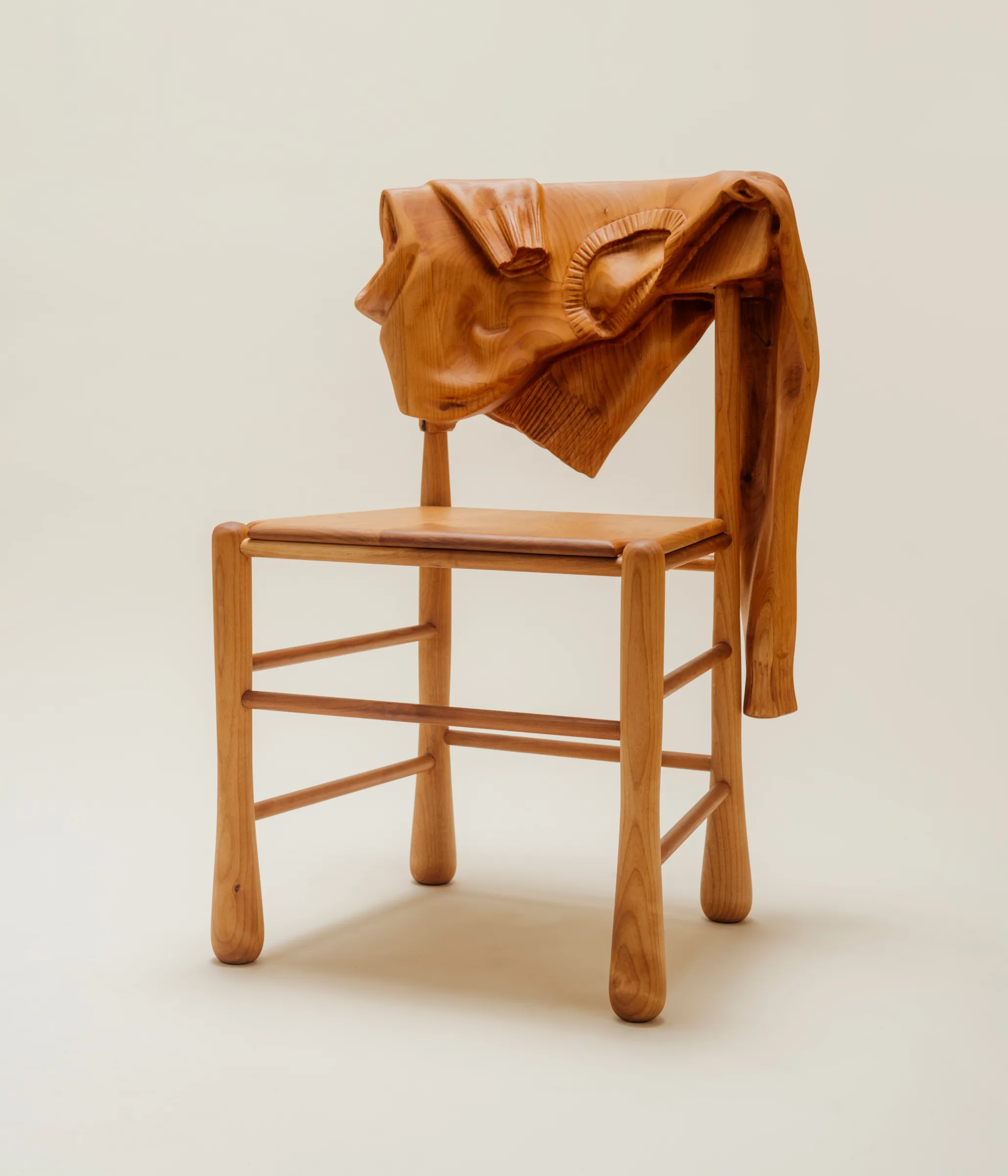 Front of wooden chair with wood sweater hanging over it on a clean background.