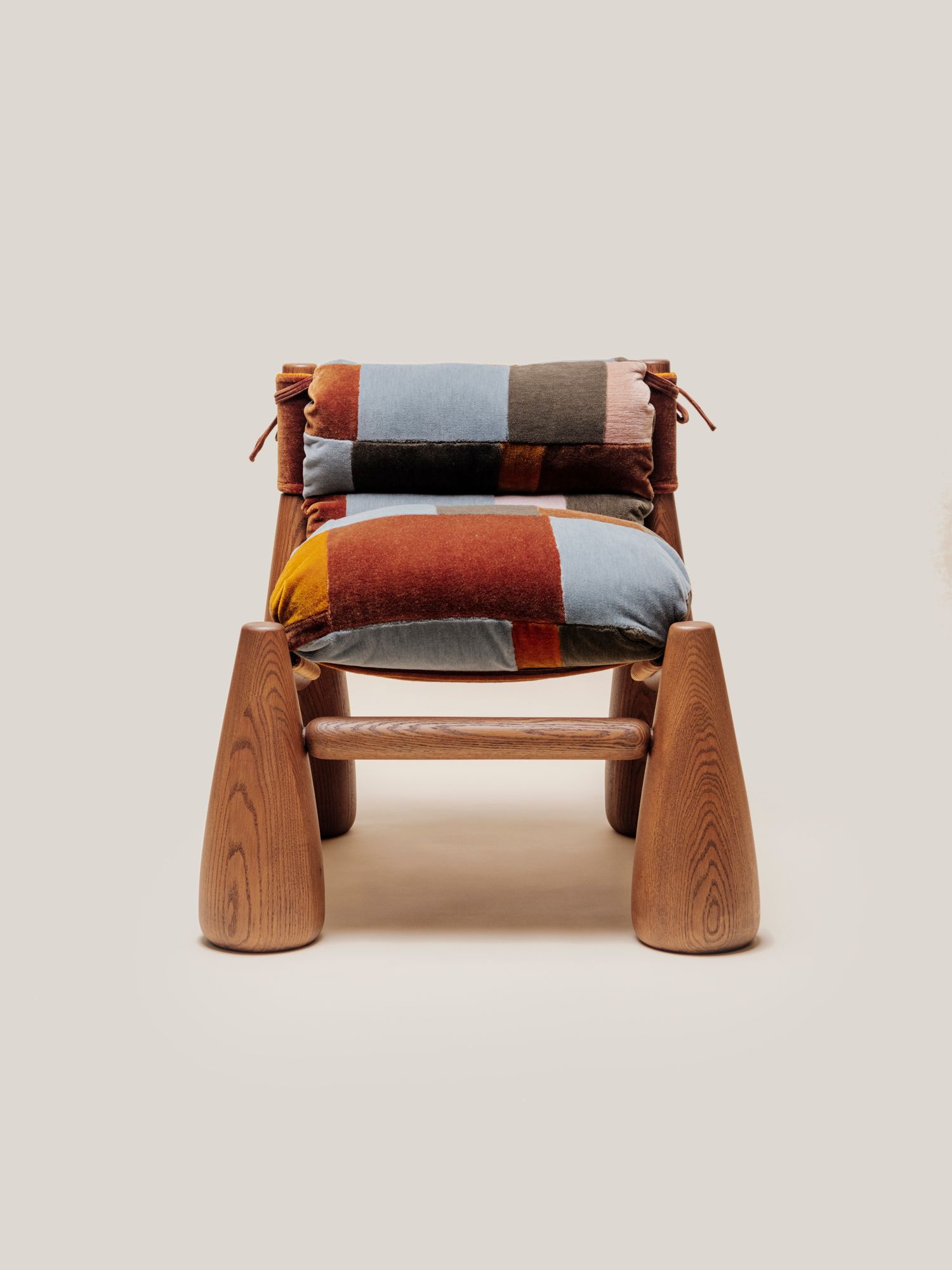 A wooden armchair with cone-shaped legs and thick, indigo patchwork cushions tied onto the frame.