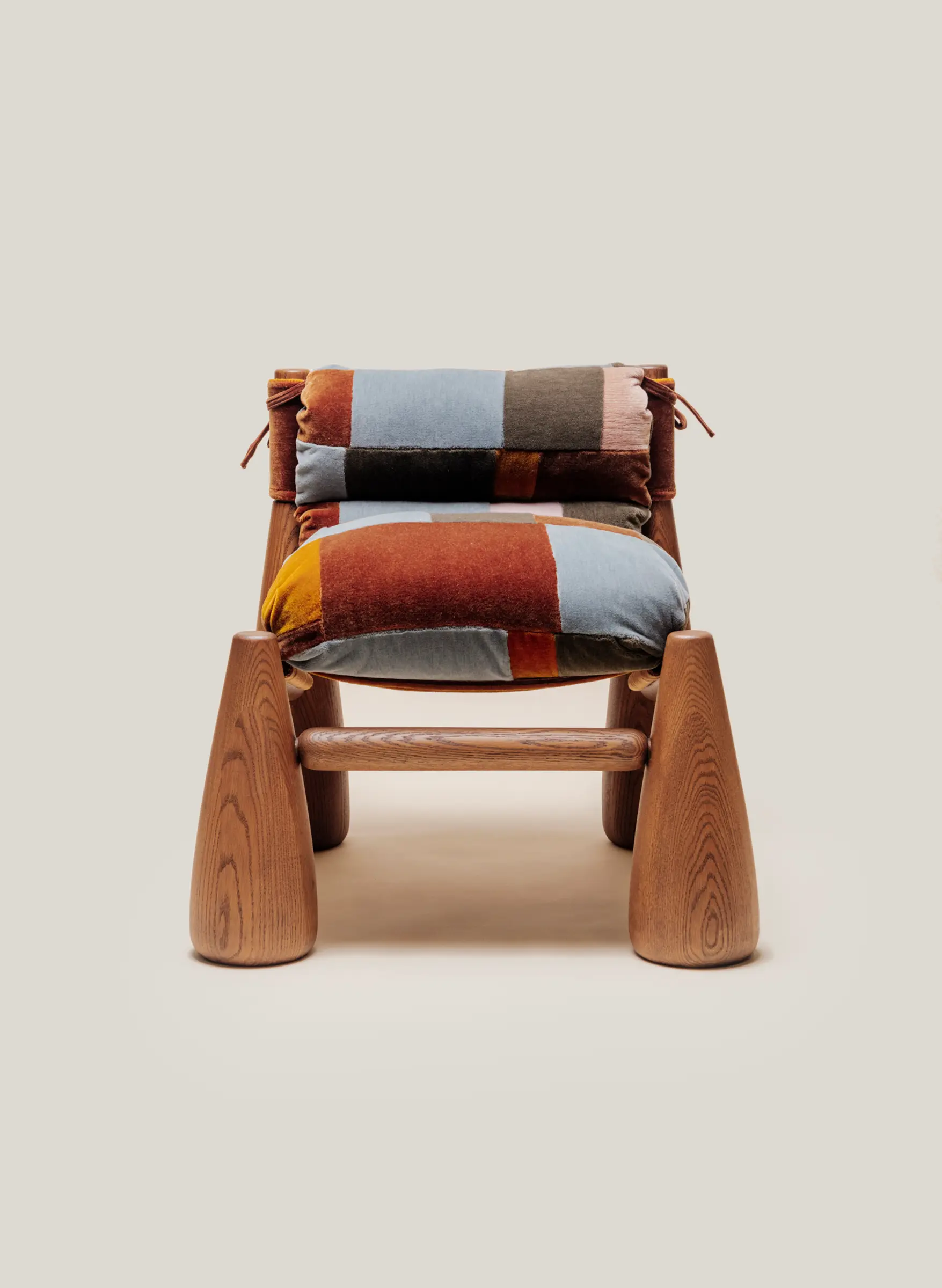 A wooden armchair with cone-shaped legs and thick, indigo patchwork cushions tied onto the frame.