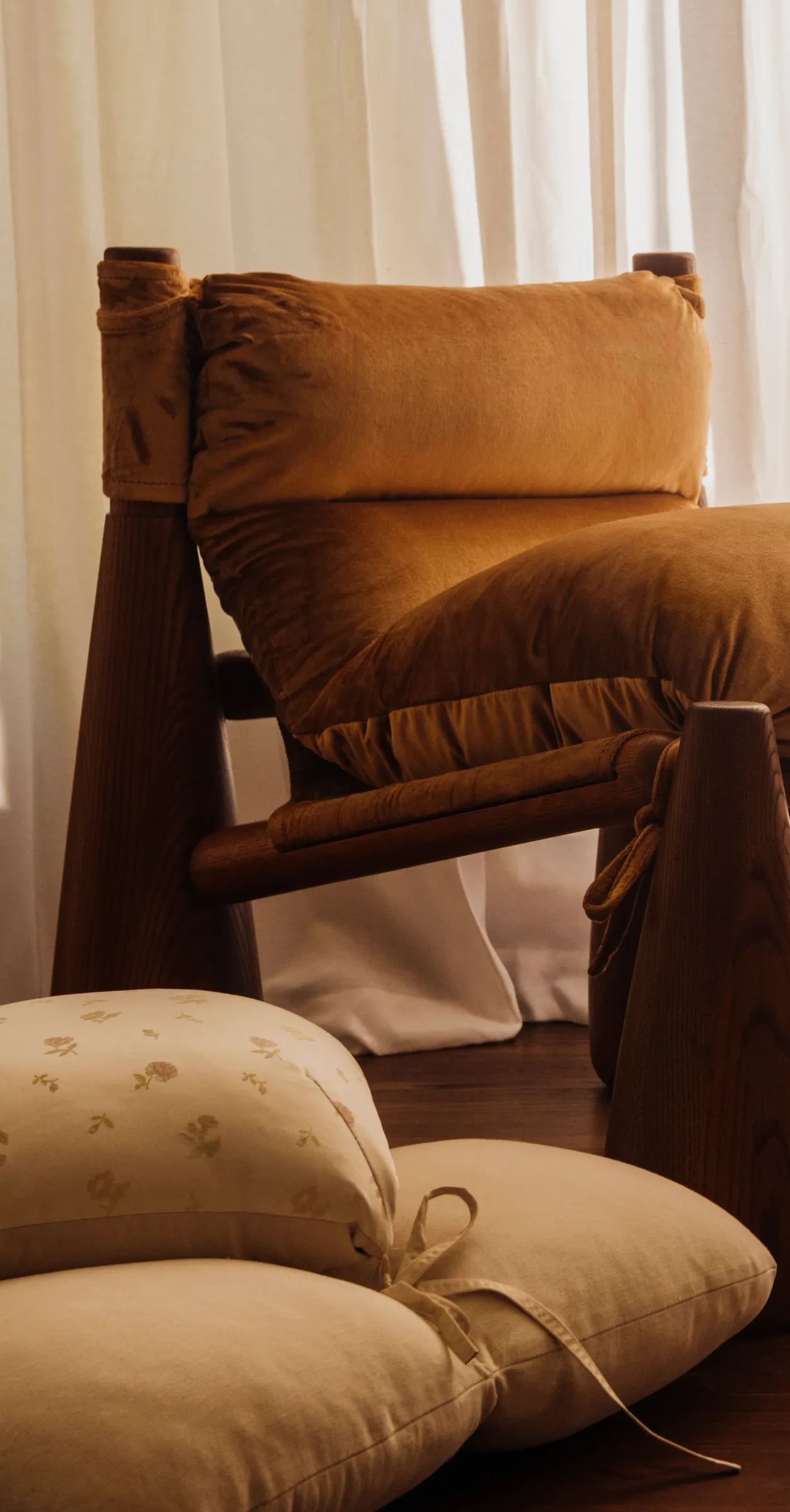 A living room with a brown Bell Chair, cushions on the floor, and a large vase of blossoming branches.