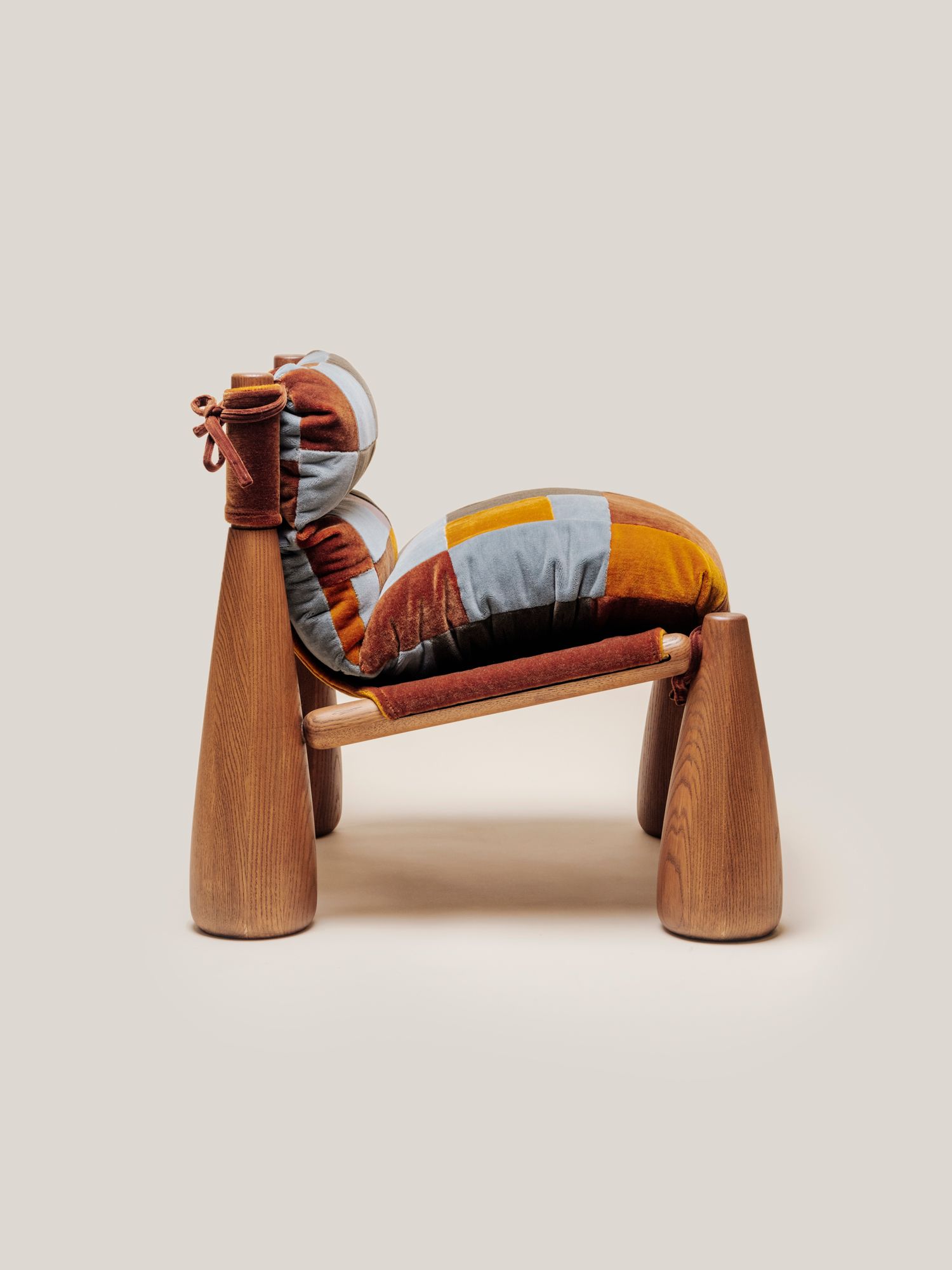 A wooden armchair with cone-shaped legs and thick, indigo patchwork cushions tied onto the frame.