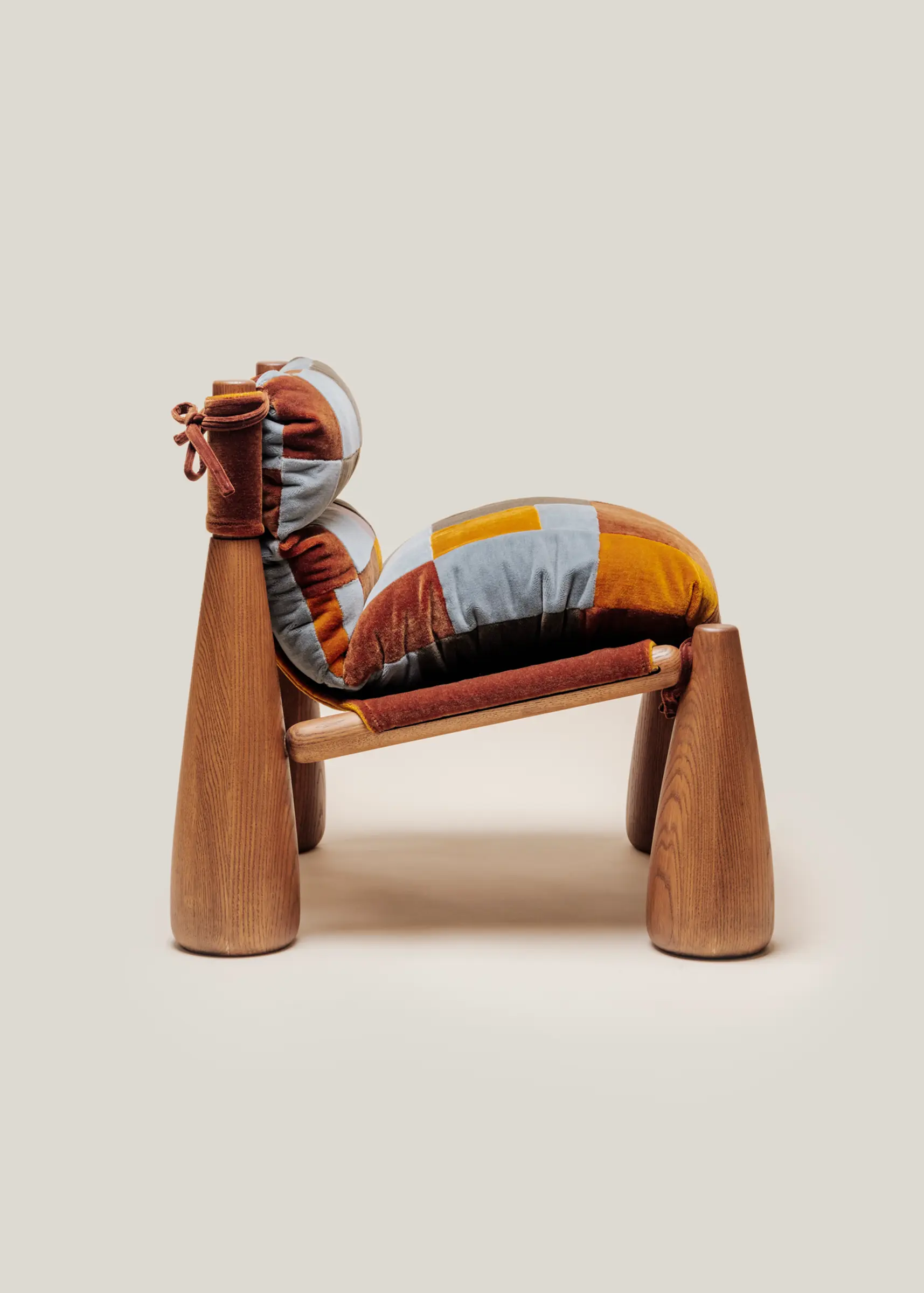 A wooden armchair with cone-shaped legs and thick, indigo patchwork cushions tied onto the frame.