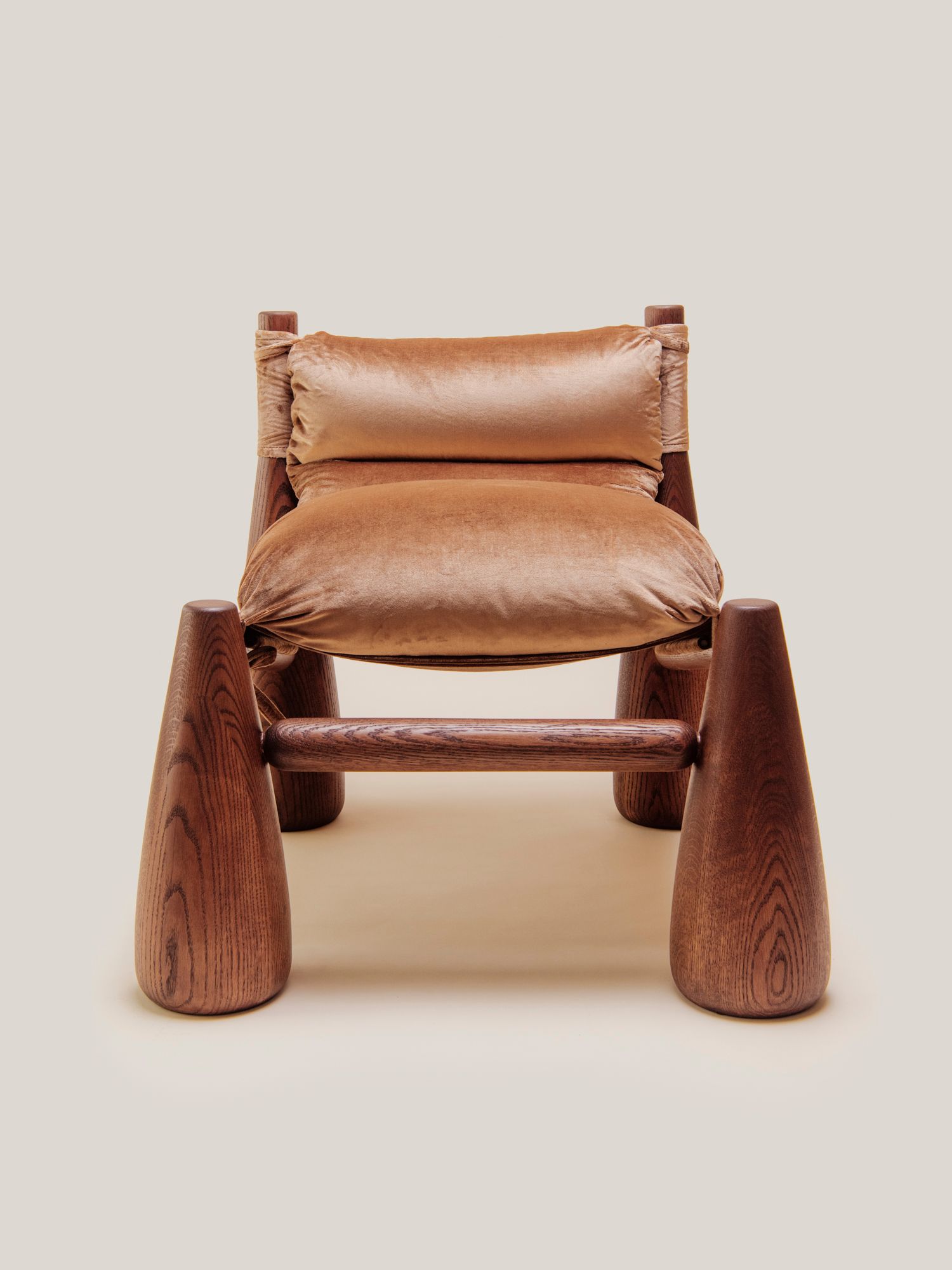 A warm-toned lounge chair with rounded wooden legs and plush velvet cushions cozy living room beside a wooden side table with a vase.