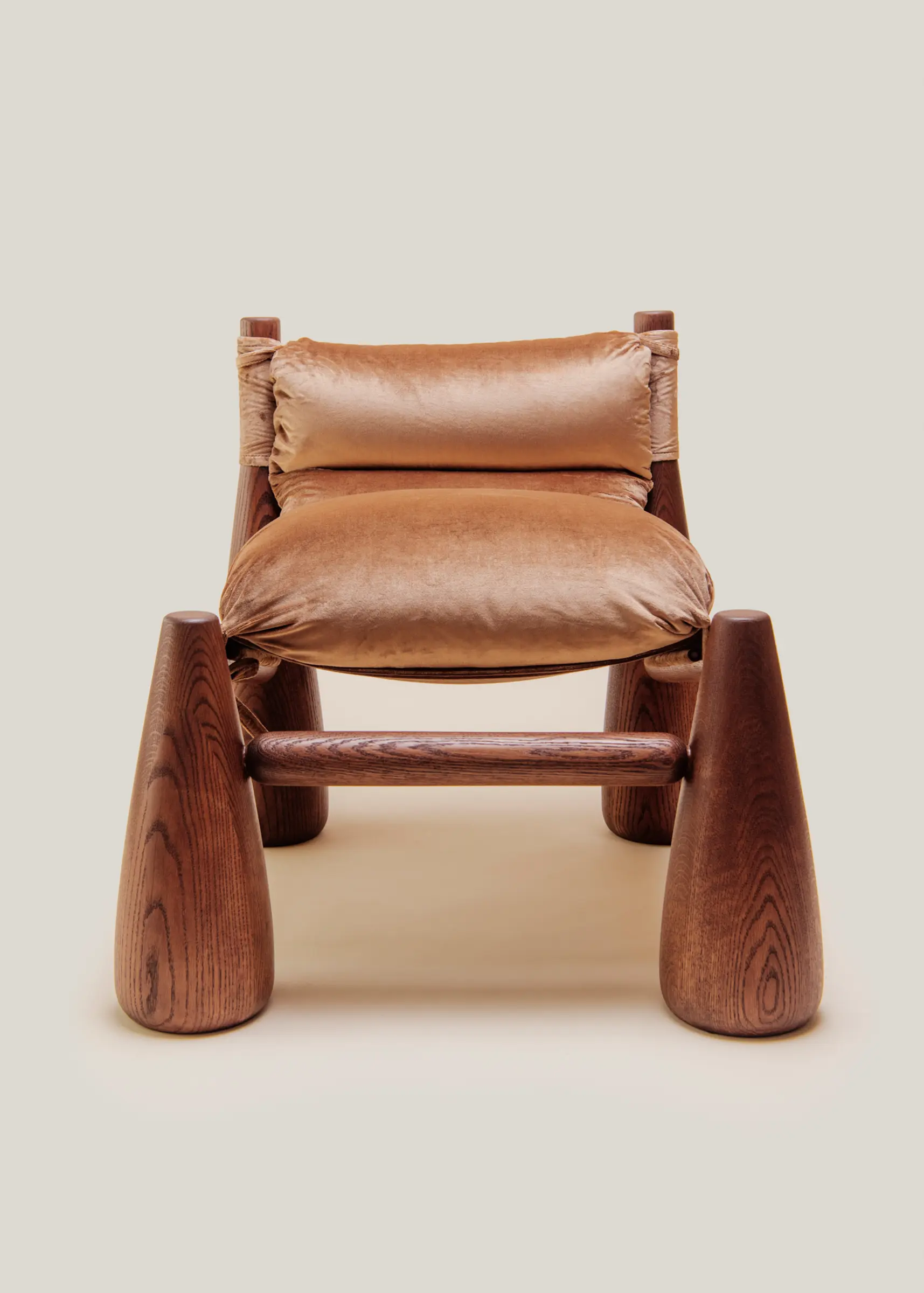 A warm-toned lounge chair with rounded wooden legs and plush velvet cushions cozy living room beside a wooden side table with a vase.