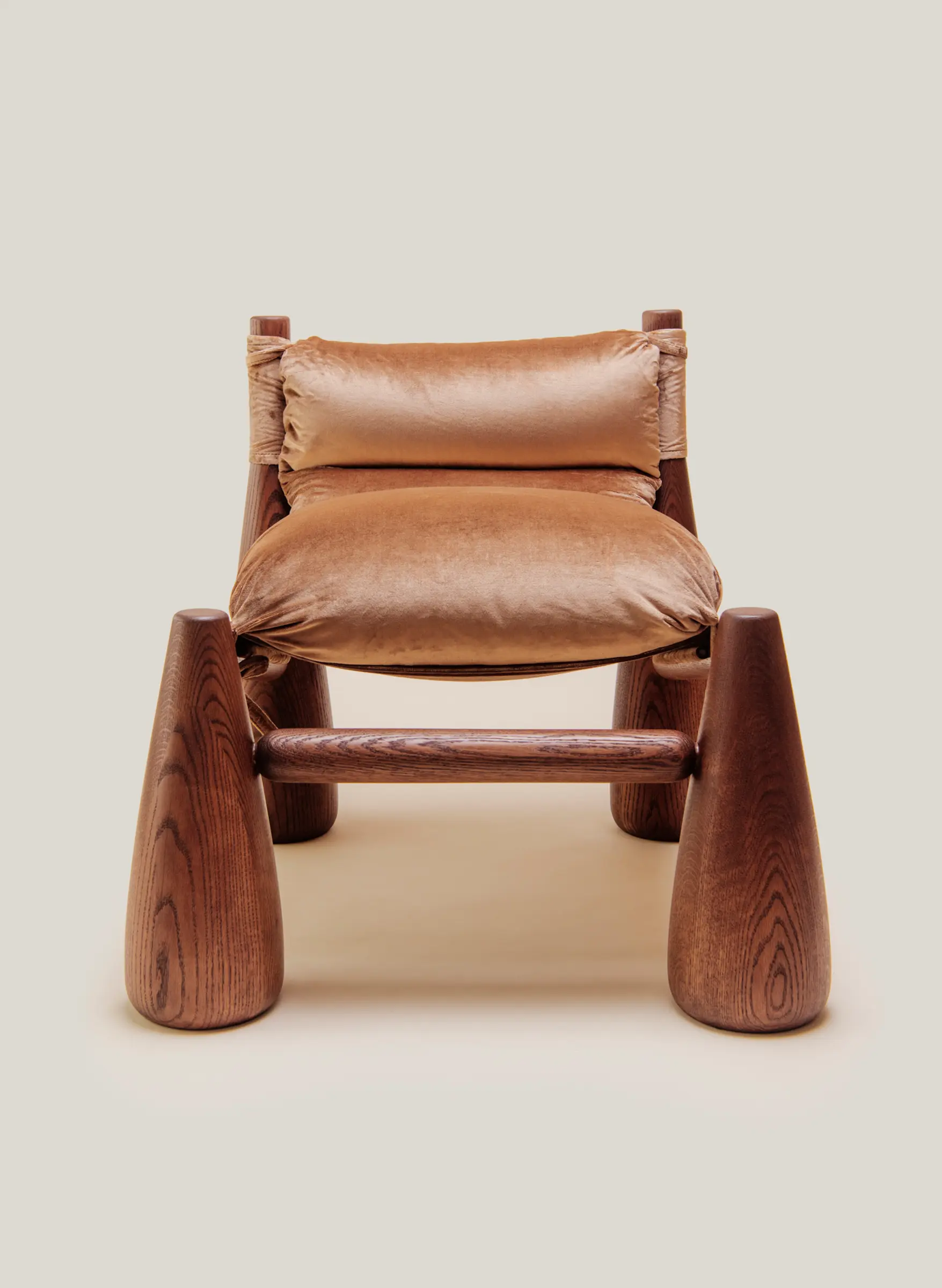 A warm-toned lounge chair with rounded wooden legs and plush velvet cushions cozy living room beside a wooden side table with a vase.