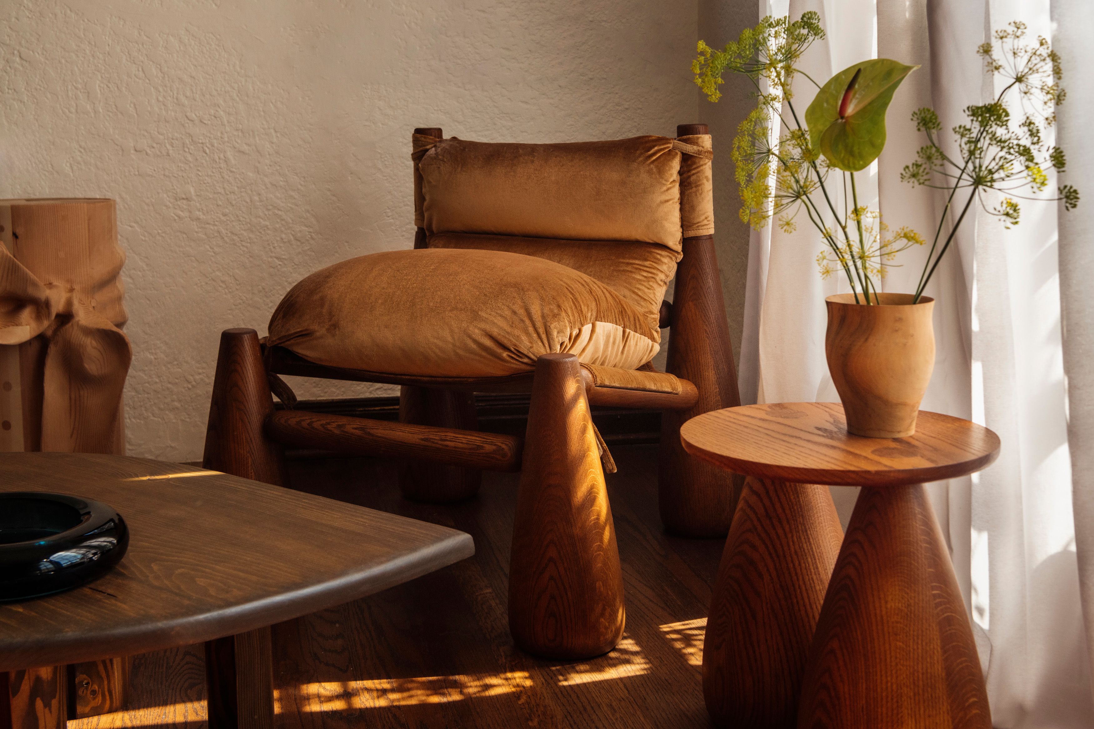 Bell chair sits in a sundrenched room next to a wood side table and petal shaped coffee table