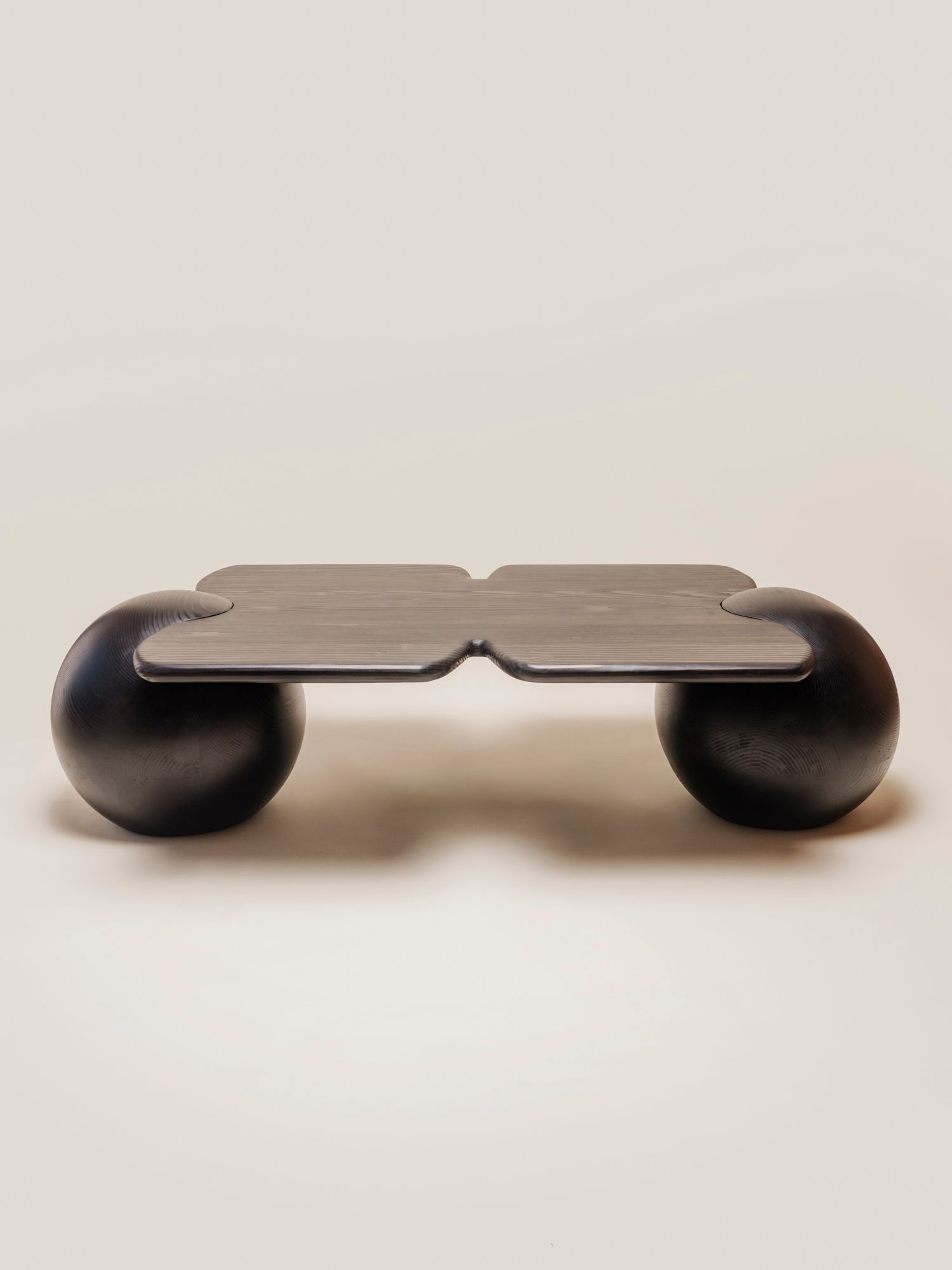 A low, sculptural black wooden table with a flat, notched top that rests on two large spherical legs.