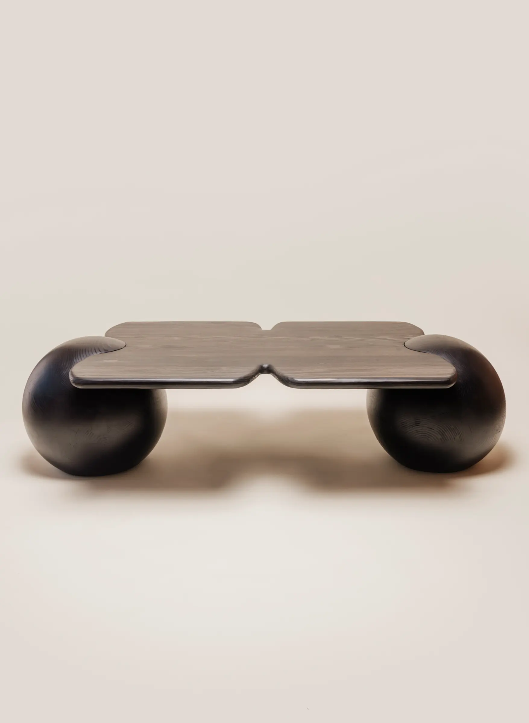 A low, sculptural black wooden table with a flat, notched top that rests on two large spherical legs.