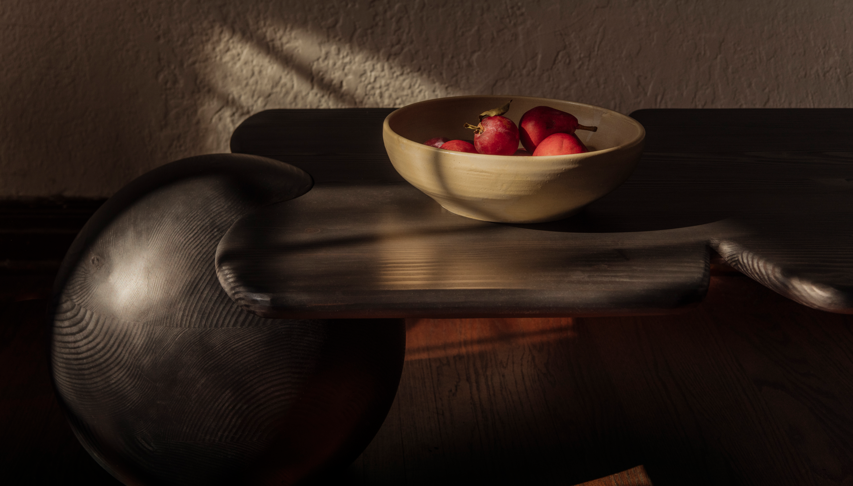 Dark wood table with ball instead of legs, soft round corners with a bowl with pears in it. 