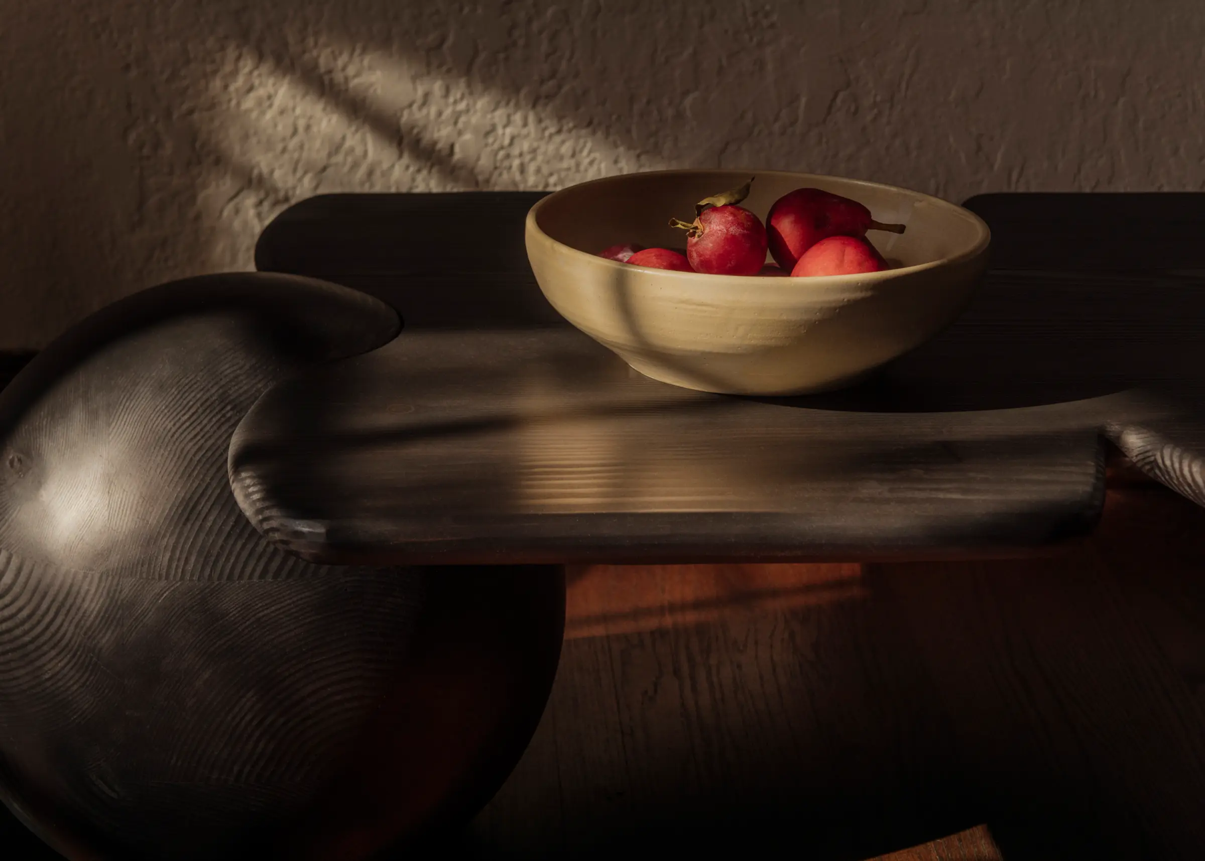 Dark wood table with ball instead of legs, soft round corners with a bowl with pears in it.