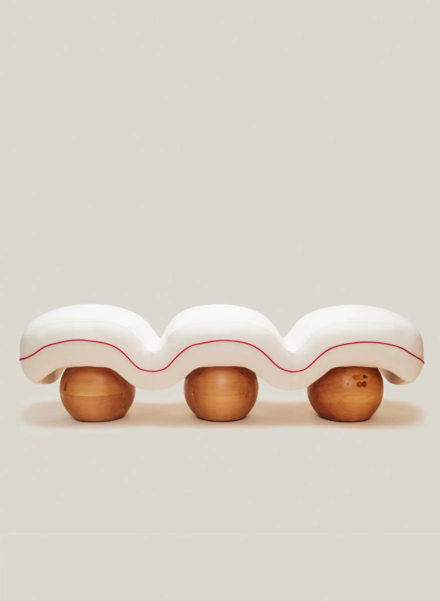 Sculptural upholstered bench with soft quilted curves and rounded wooden bases.