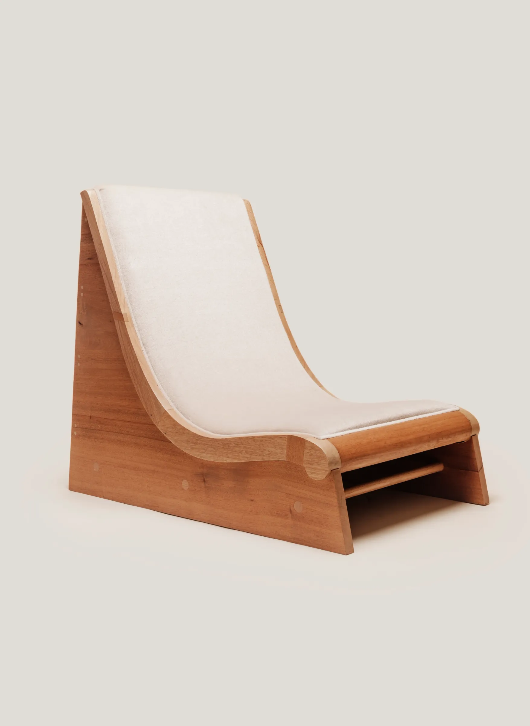A low-slung wooden lounge chair with a single, continuous white cushion that follows the S-curve of the frame.