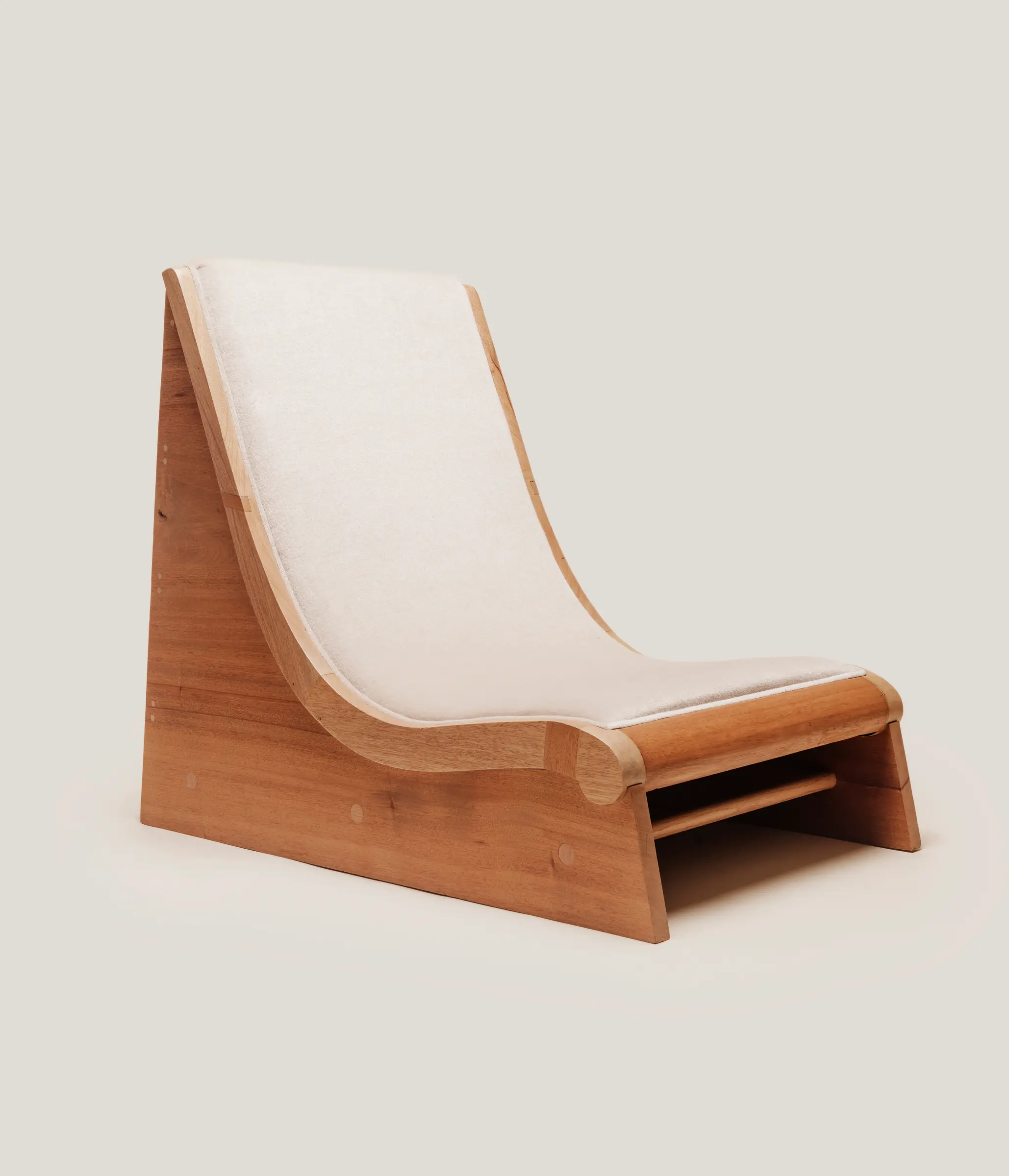 A low-slung wooden lounge chair with a single, continuous white cushion that follows the S-curve of the frame.