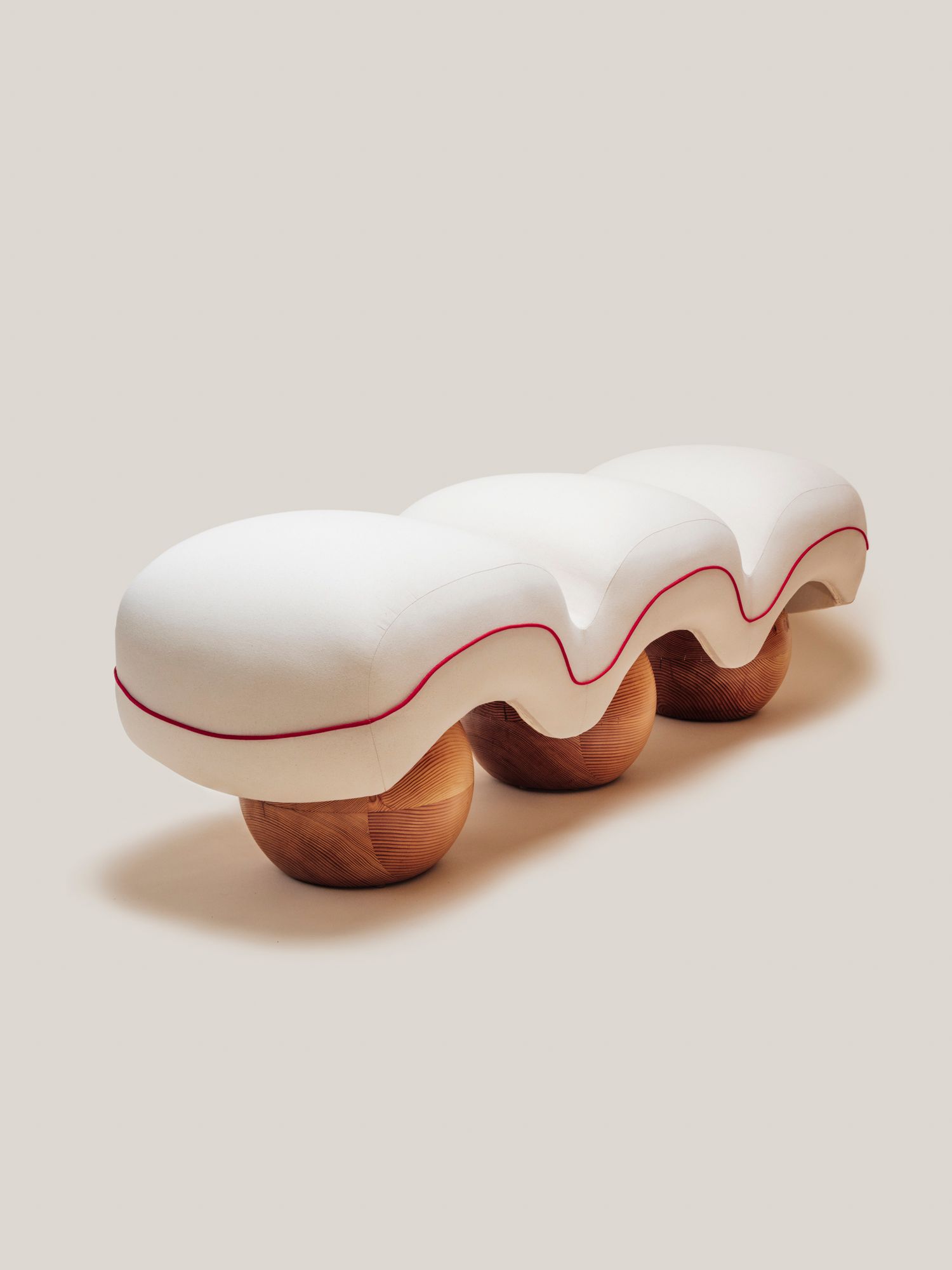 Sculptural upholstered bench with soft quilted curves and rounded wooden bases.