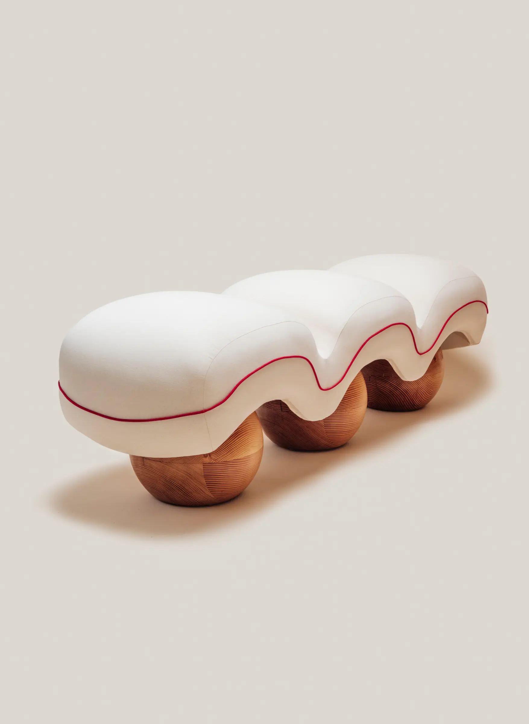Sculptural upholstered bench with soft quilted curves and rounded wooden bases.