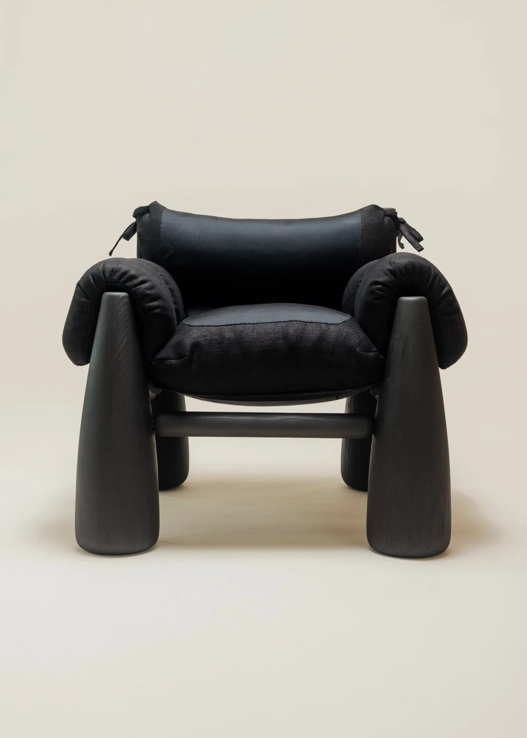 A front view of the Big Bell Chair, showcasing its modern and cozy design with a combination of black cushions and rounded black legs. The armrests and headrest are tied with black strings, emphasizing its contemporary, sculptural aesthetic.