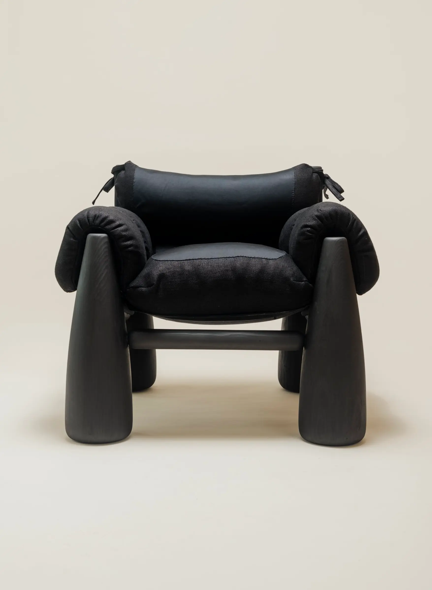 A front view of the Big Bell Chair, showcasing its modern and cozy design with a combination of black cushions and rounded black legs. The armrests and headrest are tied with black strings, emphasizing its contemporary, sculptural aesthetic.