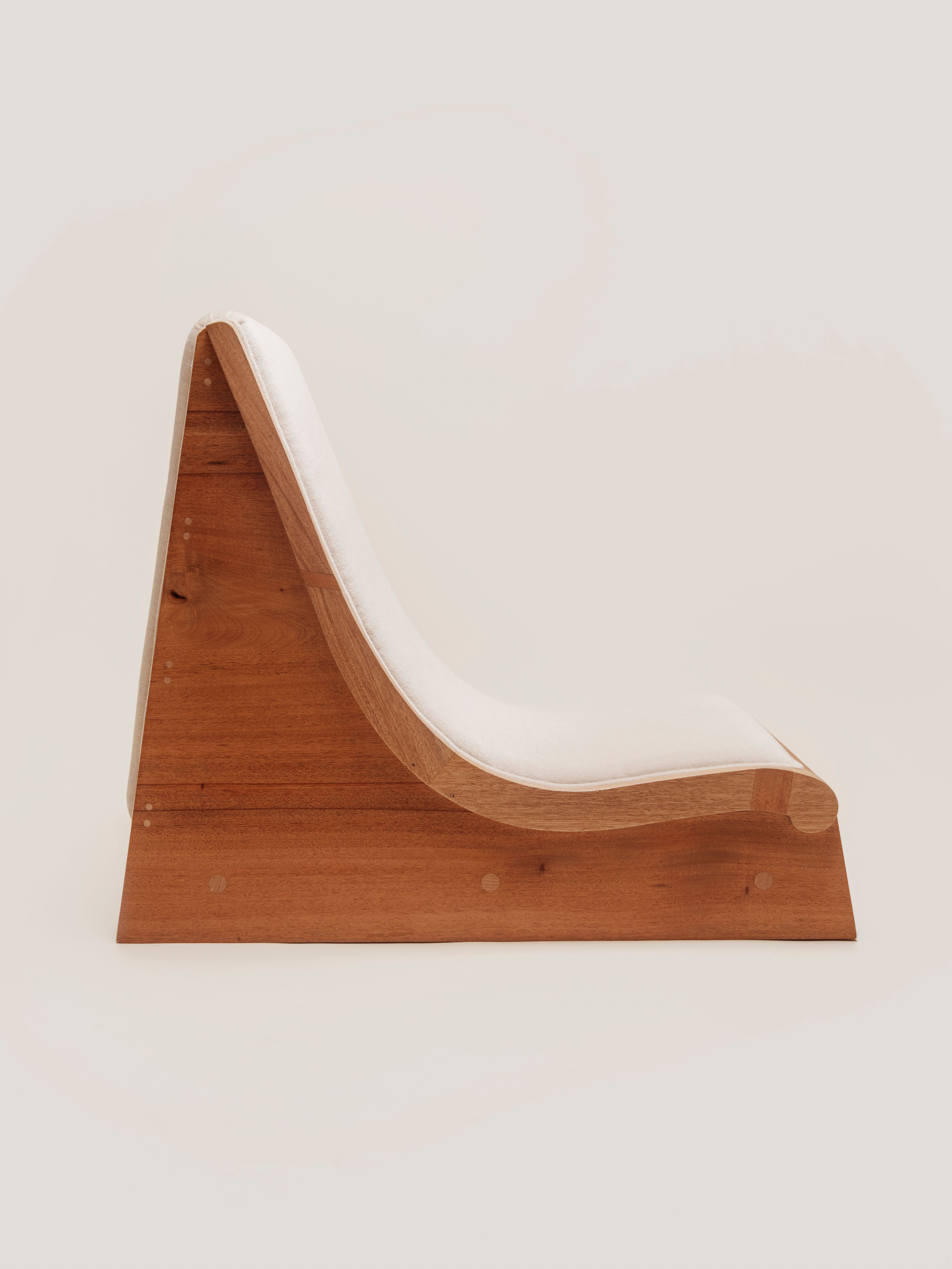 A side view of a low-slung wooden lounge chair with a single, continuous white cushion that follows the S-curve of the frame.
