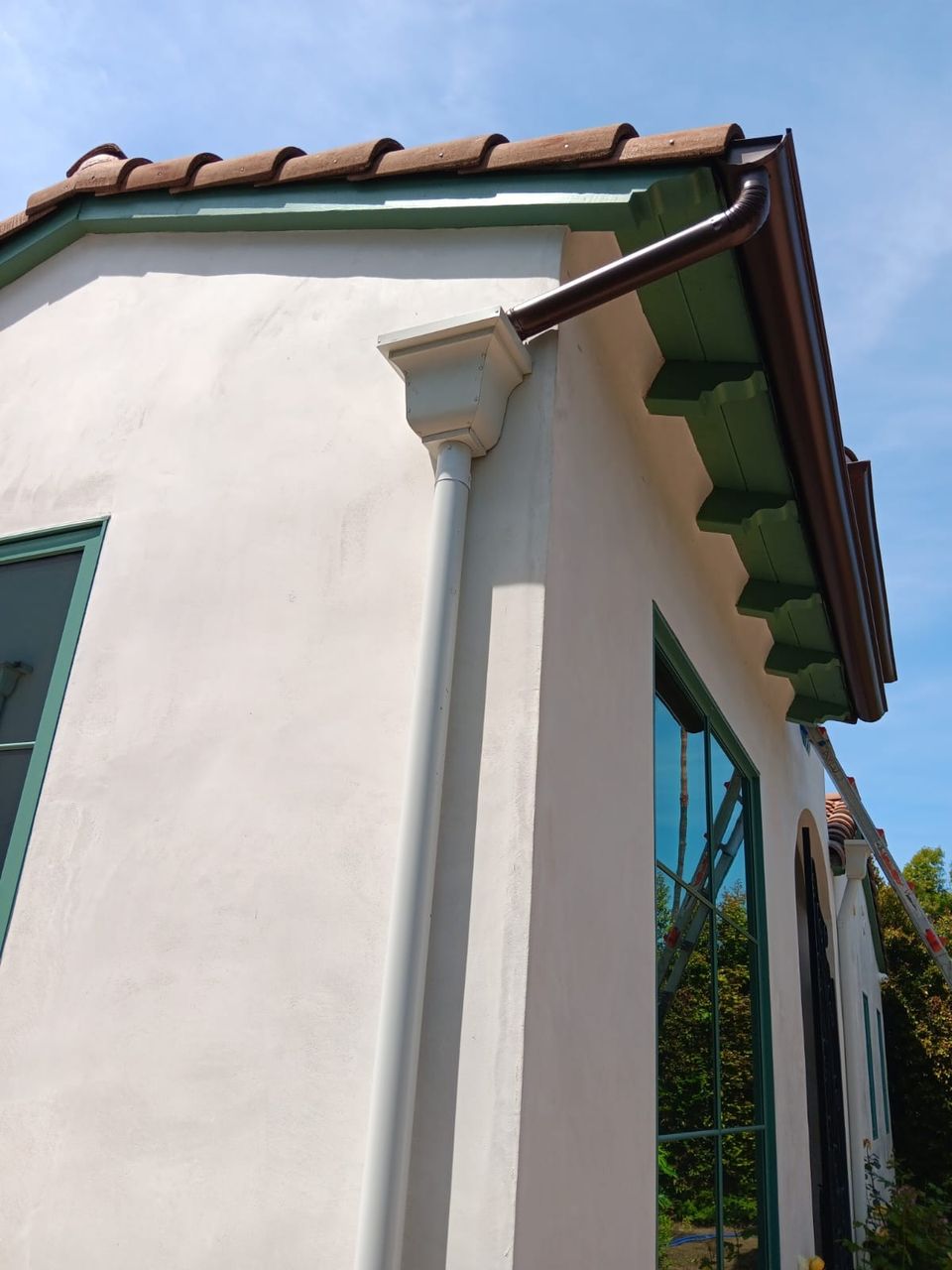 Bronze gutter following the eave of a Spanish-style home with a clay tile roof and green corbels