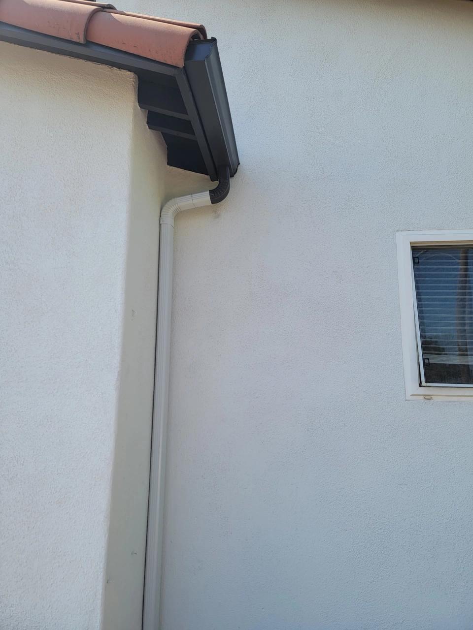 Dark bronze gutter and white downspout at the corner of a stucco home with a clay tile roof