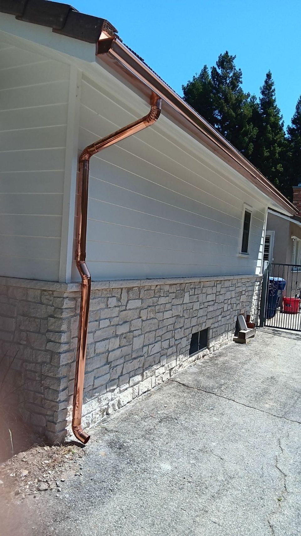 Copper downspout running down white siding to a stone foundation wall