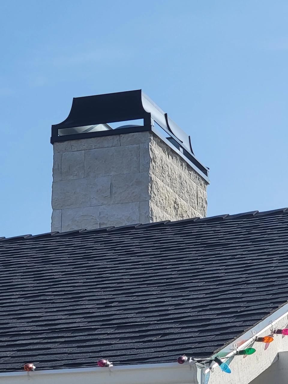 Black custom chimney shroud capping a stone chimney against a clear sky