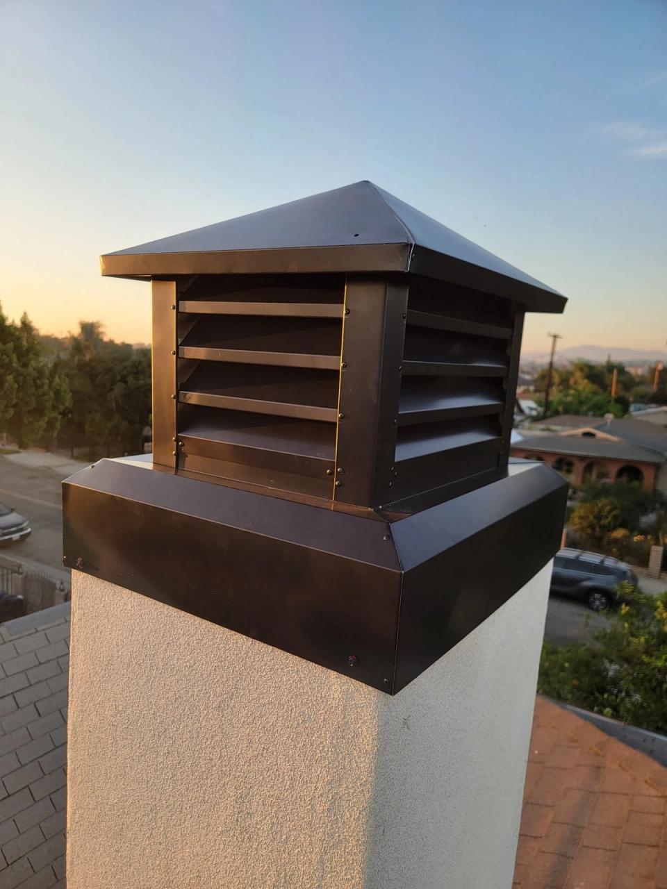 Custom bronze chimney cap with louvered vents on a stucco chimney at sunset